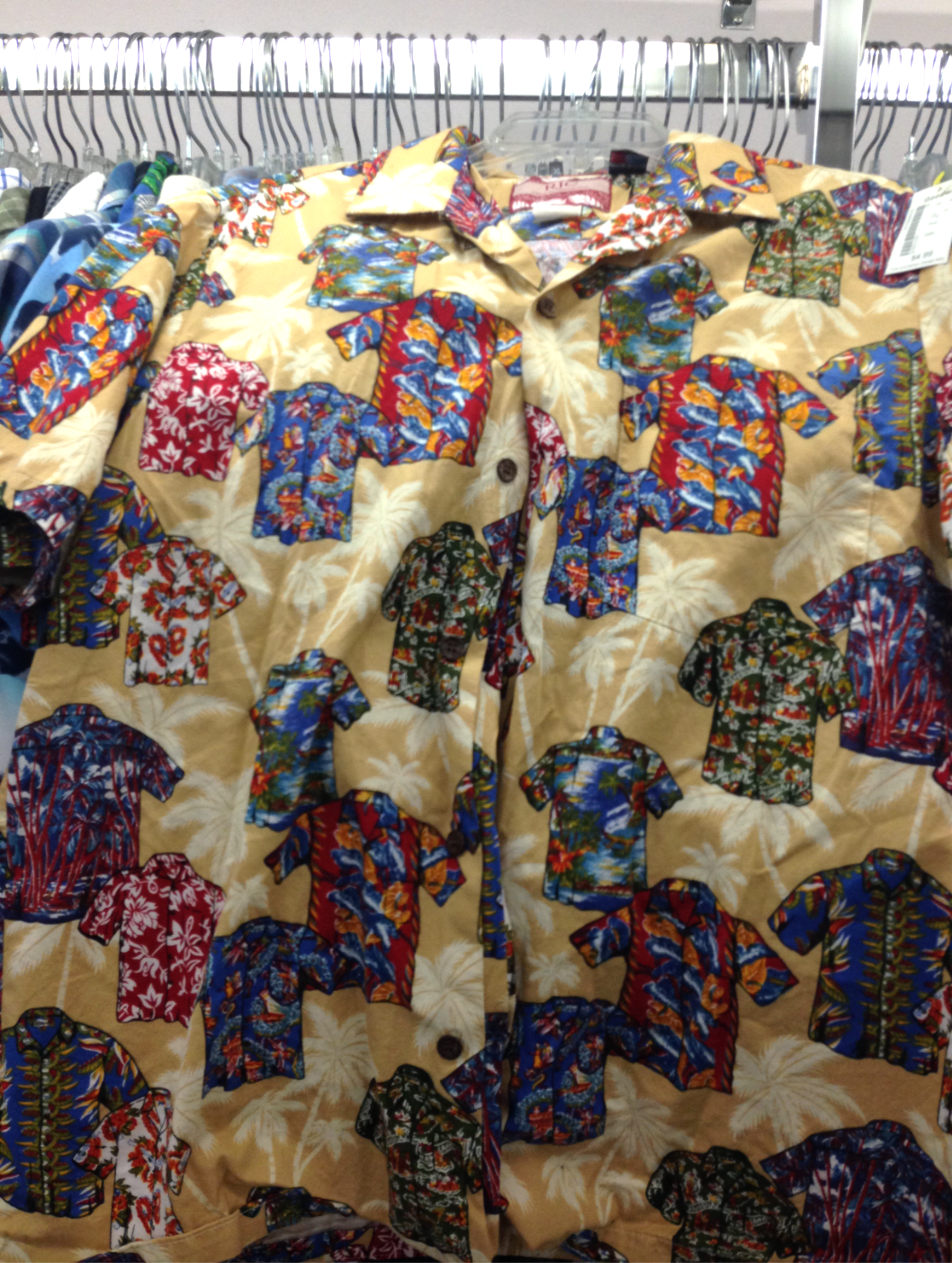 Shirt rack displaying a beige Hawaiian shirt patterned with smaller multi-colored Hawaiian shirts. Clothing store setting