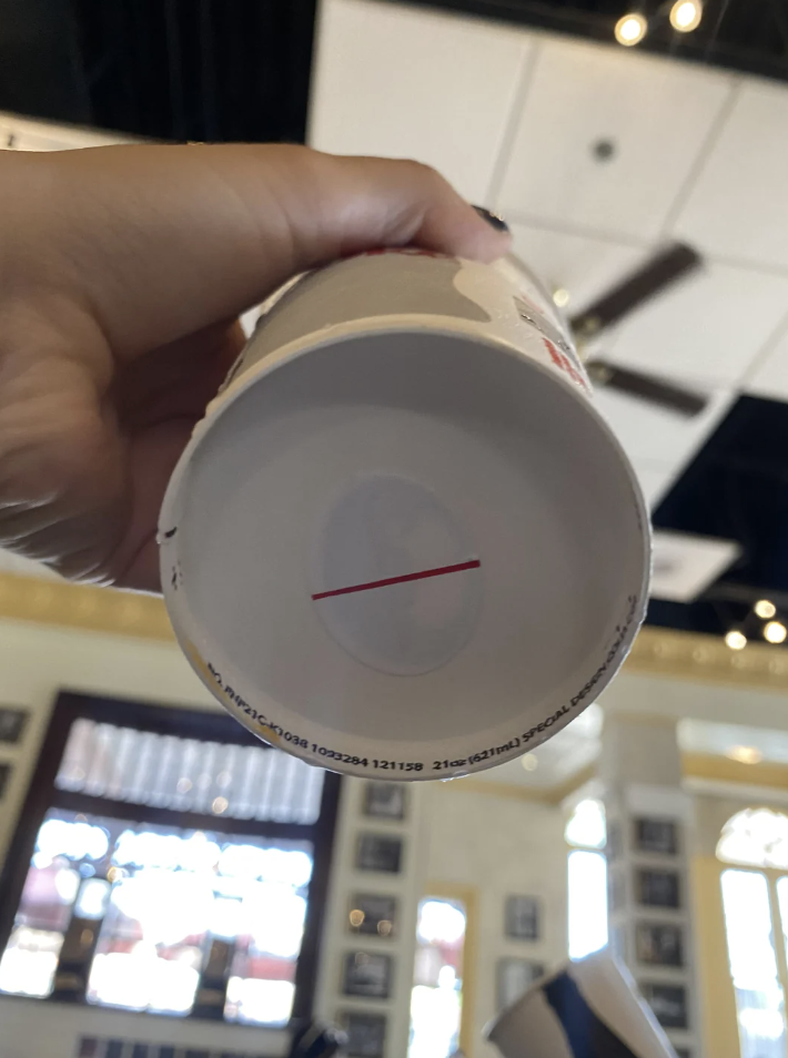 Close-up view of the bottom of a cup with an optical illusion making a white-outlined circle appear to hover above a red line. The background shows an indoor setting
