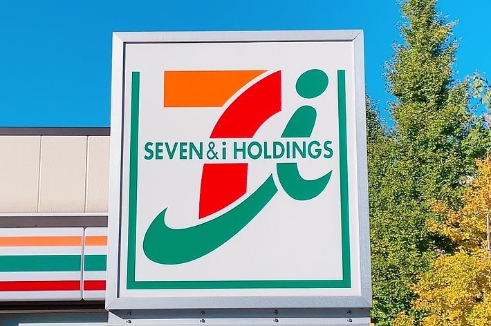 セブン&アイ・ホールディングスの看板が見えます。背景には一部の店舗外観と木々が写っています。