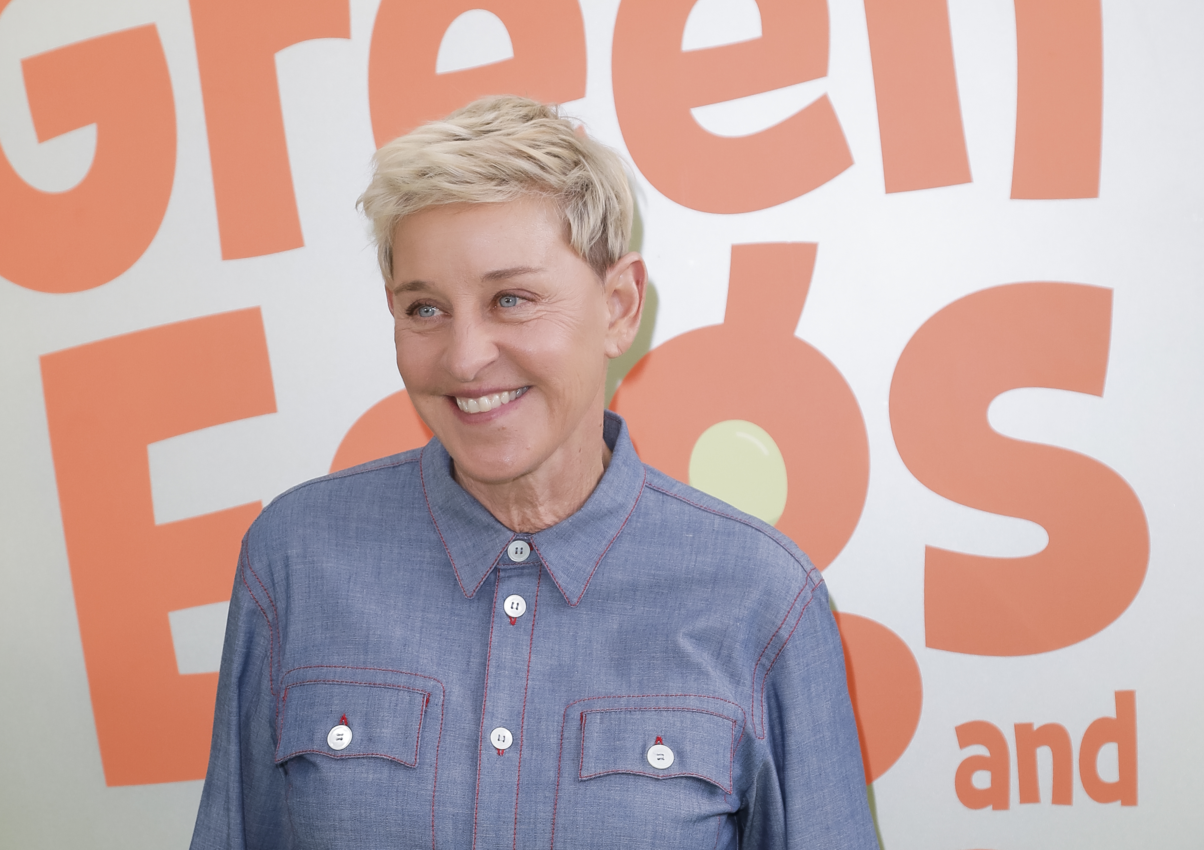 Ellen DeGeneres smiling in front of a backdrop with the text "Green Eggs and …"