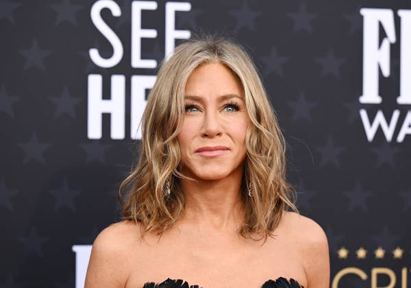 Jennifer Aniston on the red carpet at an event. She has wavy hair and is wearing an elegant, strapless outfit