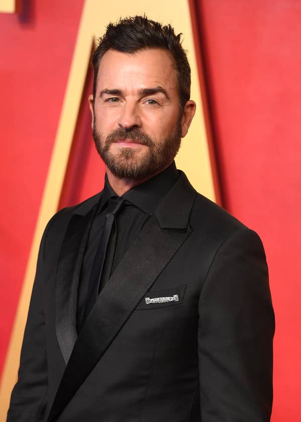 Justin Theroux on the red carpet wearing a dark suit with a dark tie