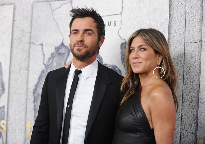 Jennifer Aniston in a one-shoulder dress and Justin Theroux in a suit, pose together at a red carpet event