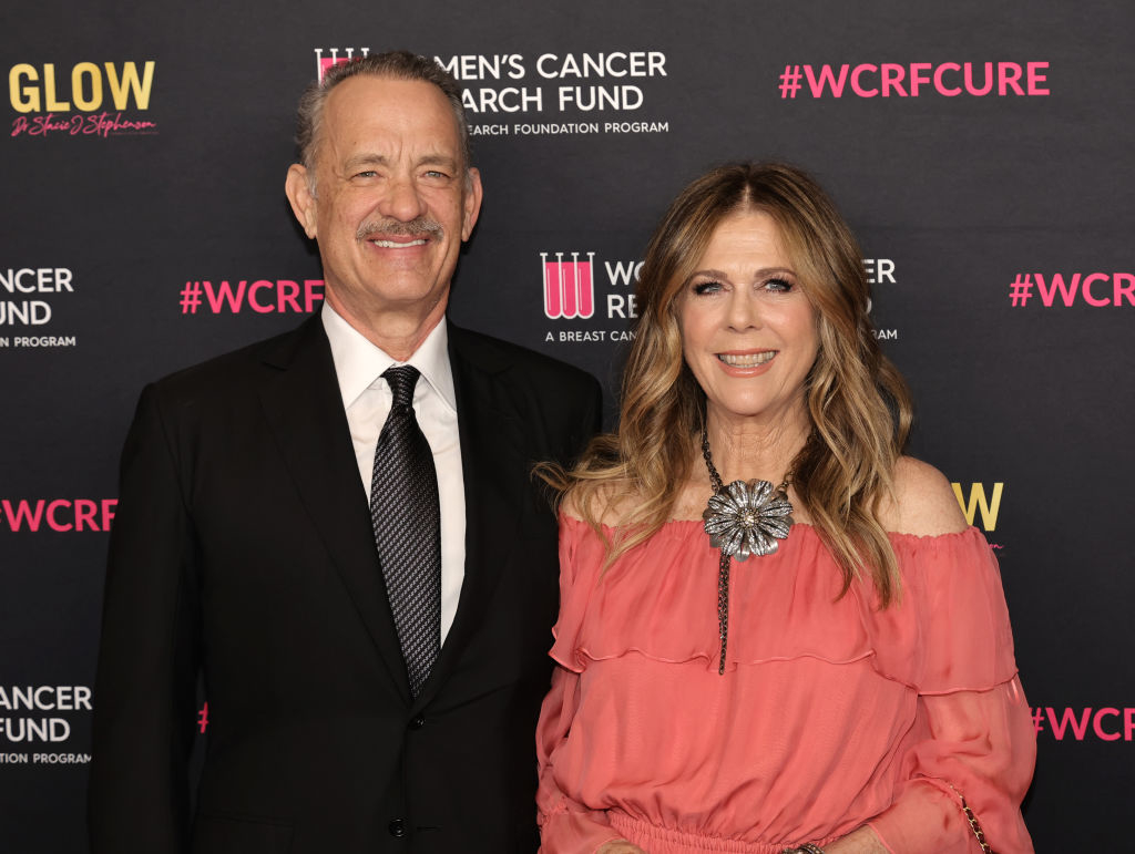 Tom Hanks in a suit and Rita Wilson in an off-the-shoulder dress at Women's Cancer Research Fund event, posing in front of a branded backdrop