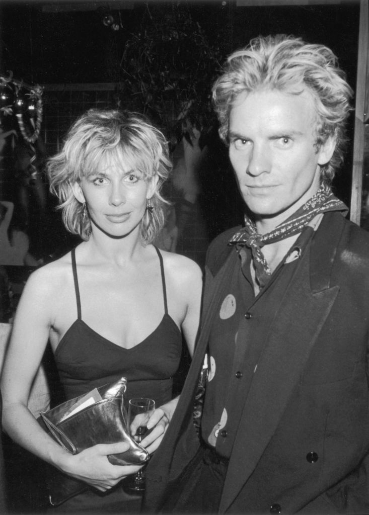 Trudie Styler and Sting at an event, with Trudie in a sleeveless dress and Sting in a suit with a patterned shirt and scarf