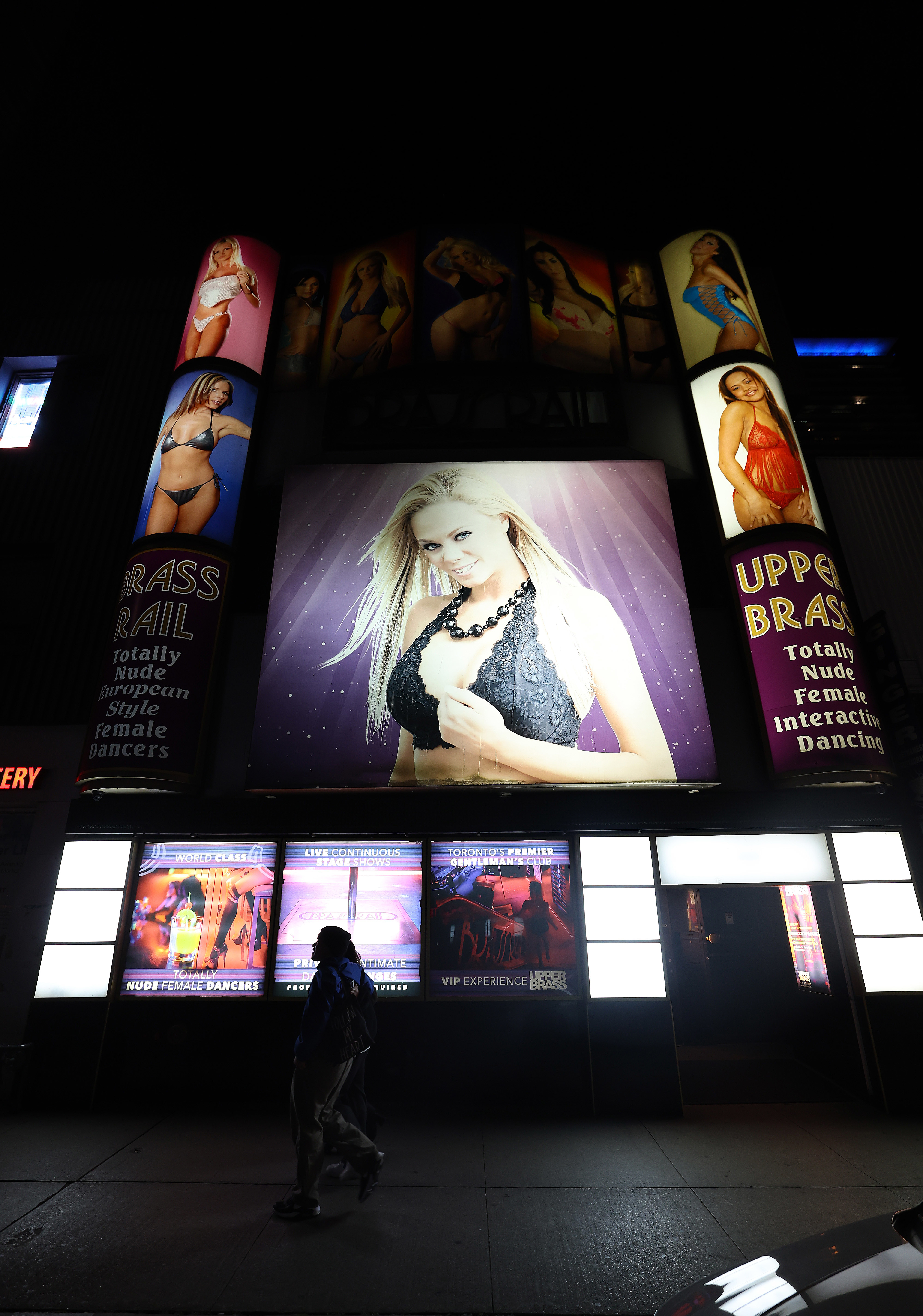 A street view of Upper Brass, an adult entertainment club promoting totally nude female dancers, with illuminated posters of provocative models