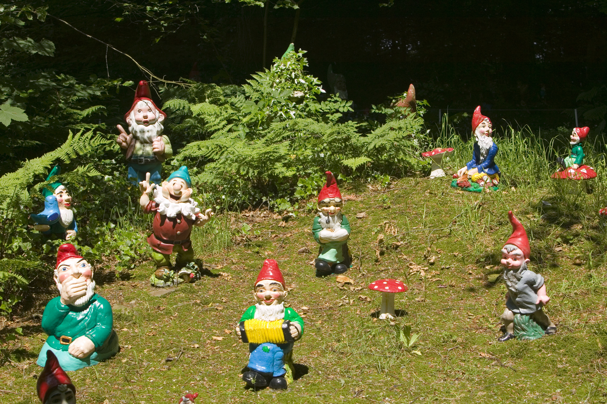 Several gnome statues with distinct poses and expressions are scattered across a grassy, foliage-rich garden area