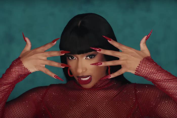 Megan poses with long nails and a mesh outfit, holding her hands near her face with an intense and confident expression