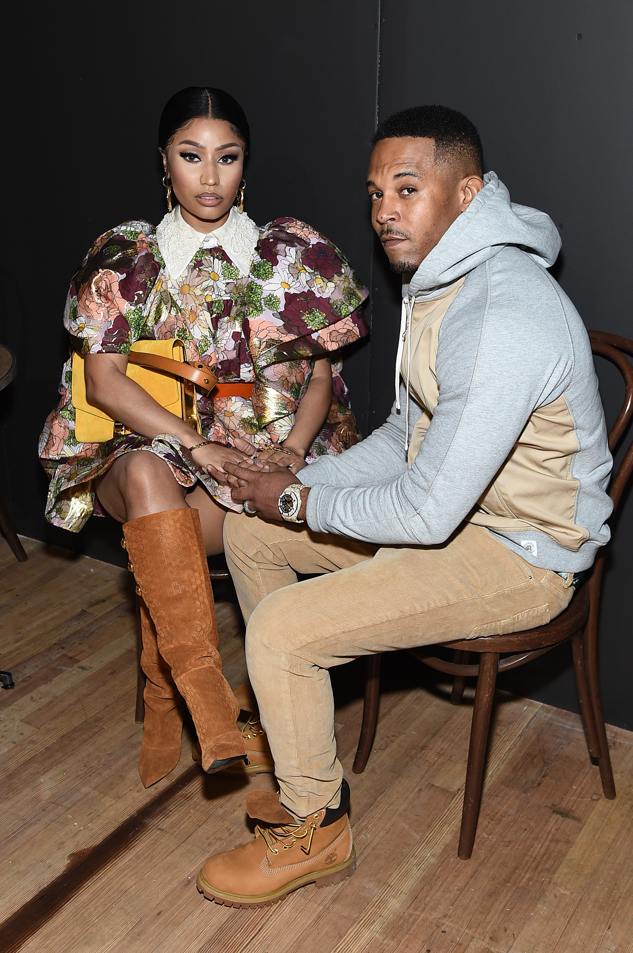 Nicki Minaj in a floral dress with puffed sleeves and boots, sitting beside Kenneth Petty in casual attire, holding hands in a seated pose