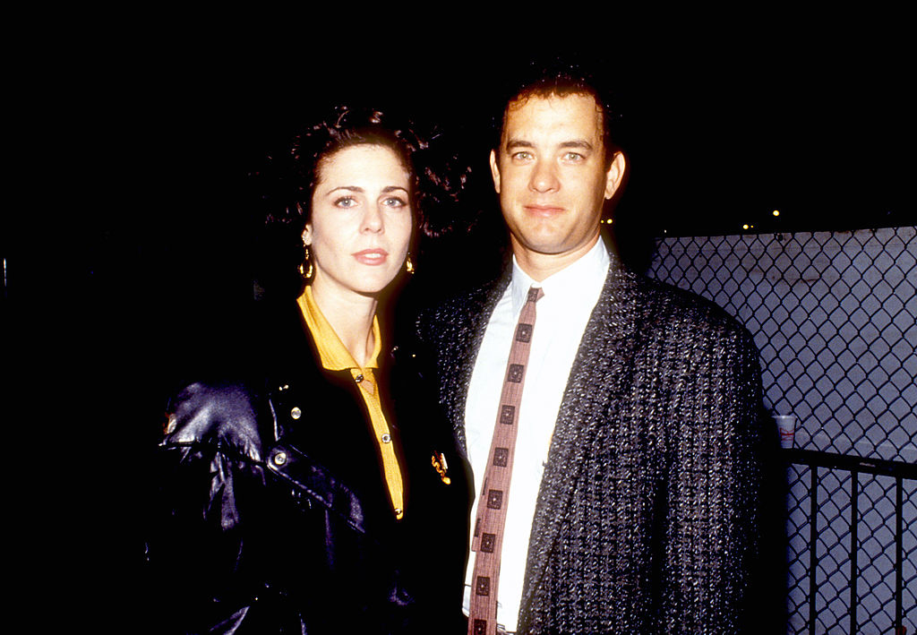 Rita Wilson and Tom Hanks on the red carpet. Rita is wearing a leather jacket over a blouse, and Tom is in a suit with a patterned tie
