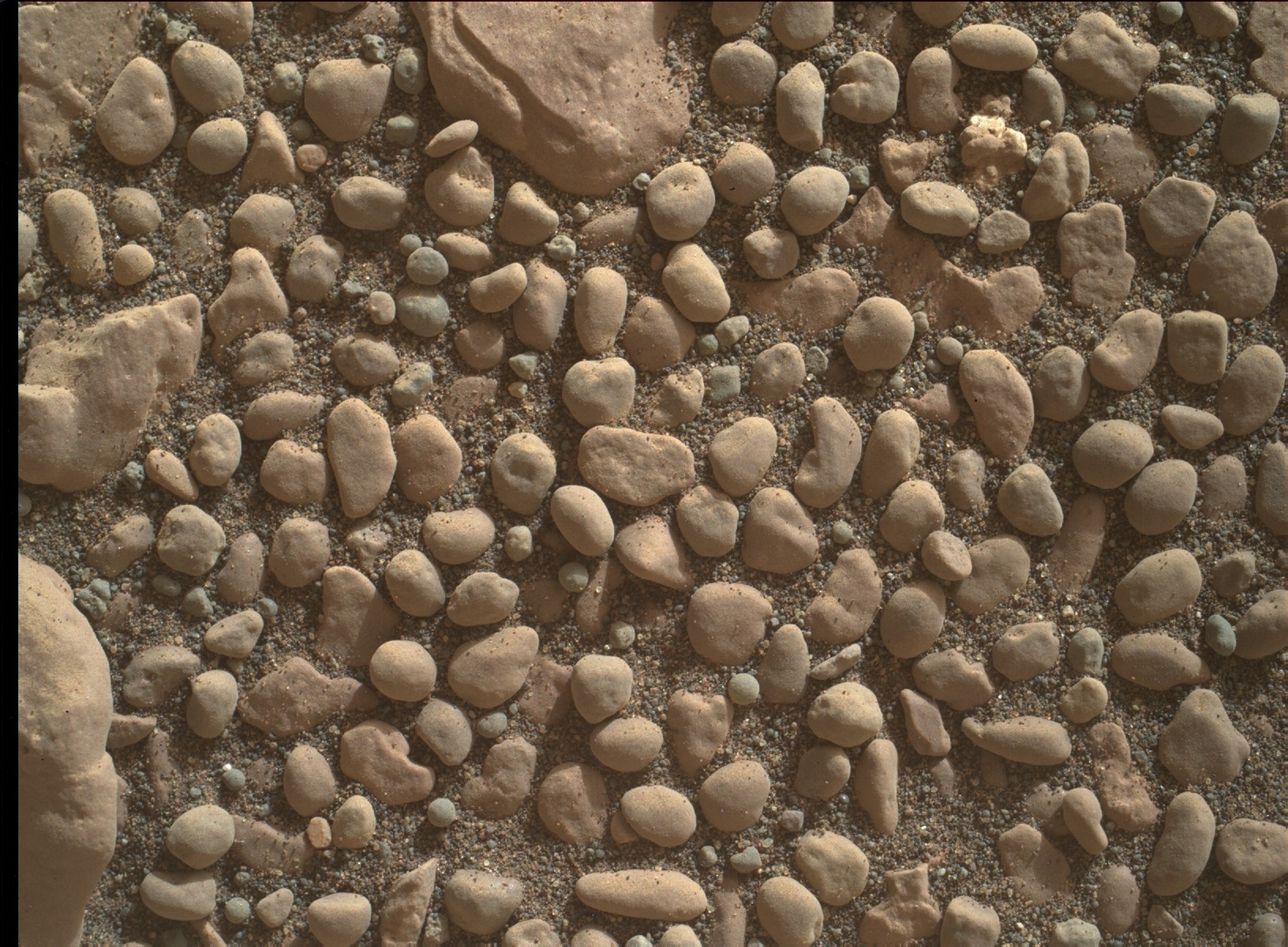 Various sizes of small and large pebbles are scattered on a sandy surface