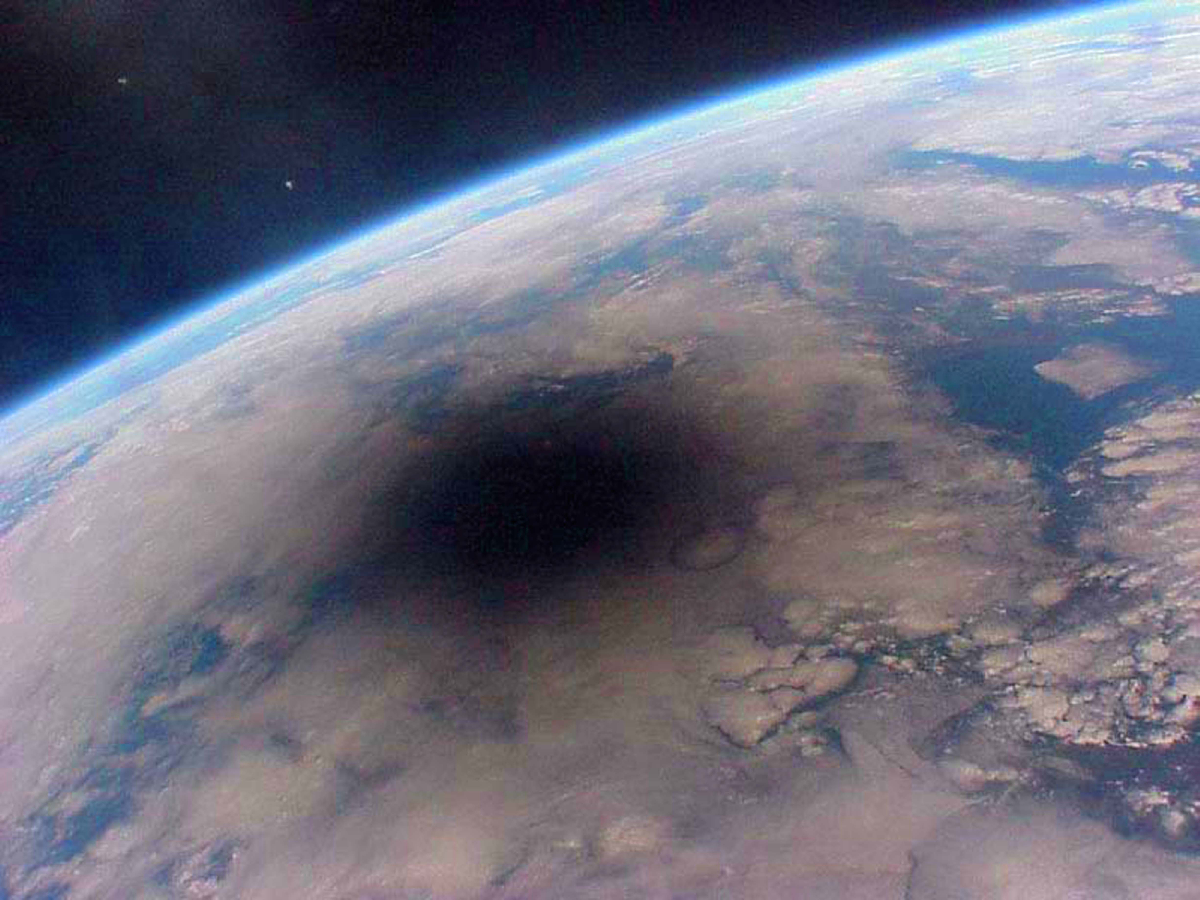 View of Earth from space showing a large shadow, likely from a solar eclipse, covering parts of the surface. The horizon of the planet curves in the distance