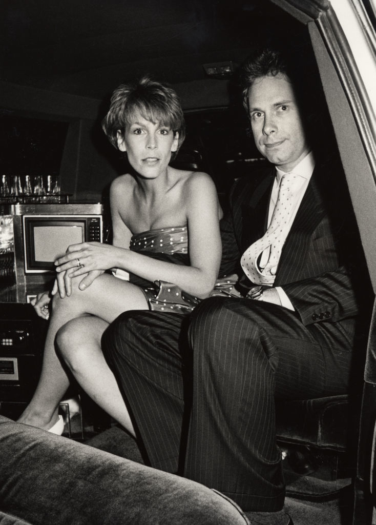 Jamie Lee Curtis in a strapless dress and Christopher Guest in a pinstripe suit sitting together in a limousine