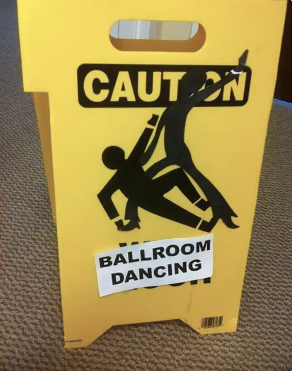 Yellow caution sign with a graphic of people ballroom dancing and a label "BALLROOM DANCING" covering the word "WET."