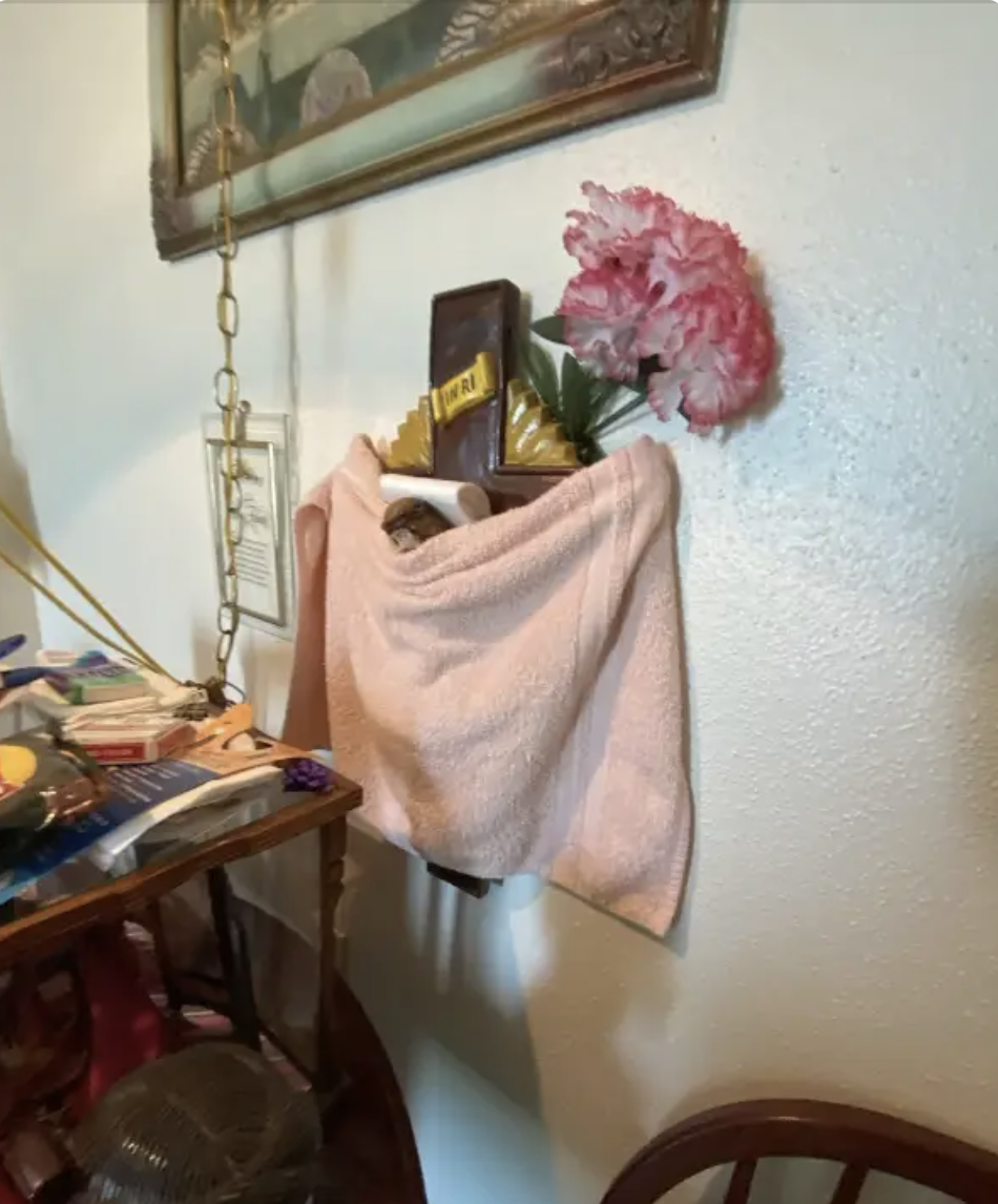 A small altar on a wall featuring various items, including flowers, a towel, and religious figurines, next to a cluttered table