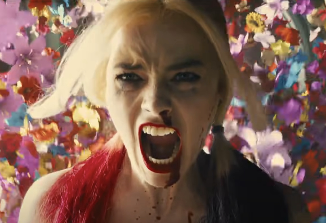 Margot Robbie as Harley Quinn, with an intense expression, mouth open, vibrant flowers in the background, from a scene in "Birds of Prey" movie