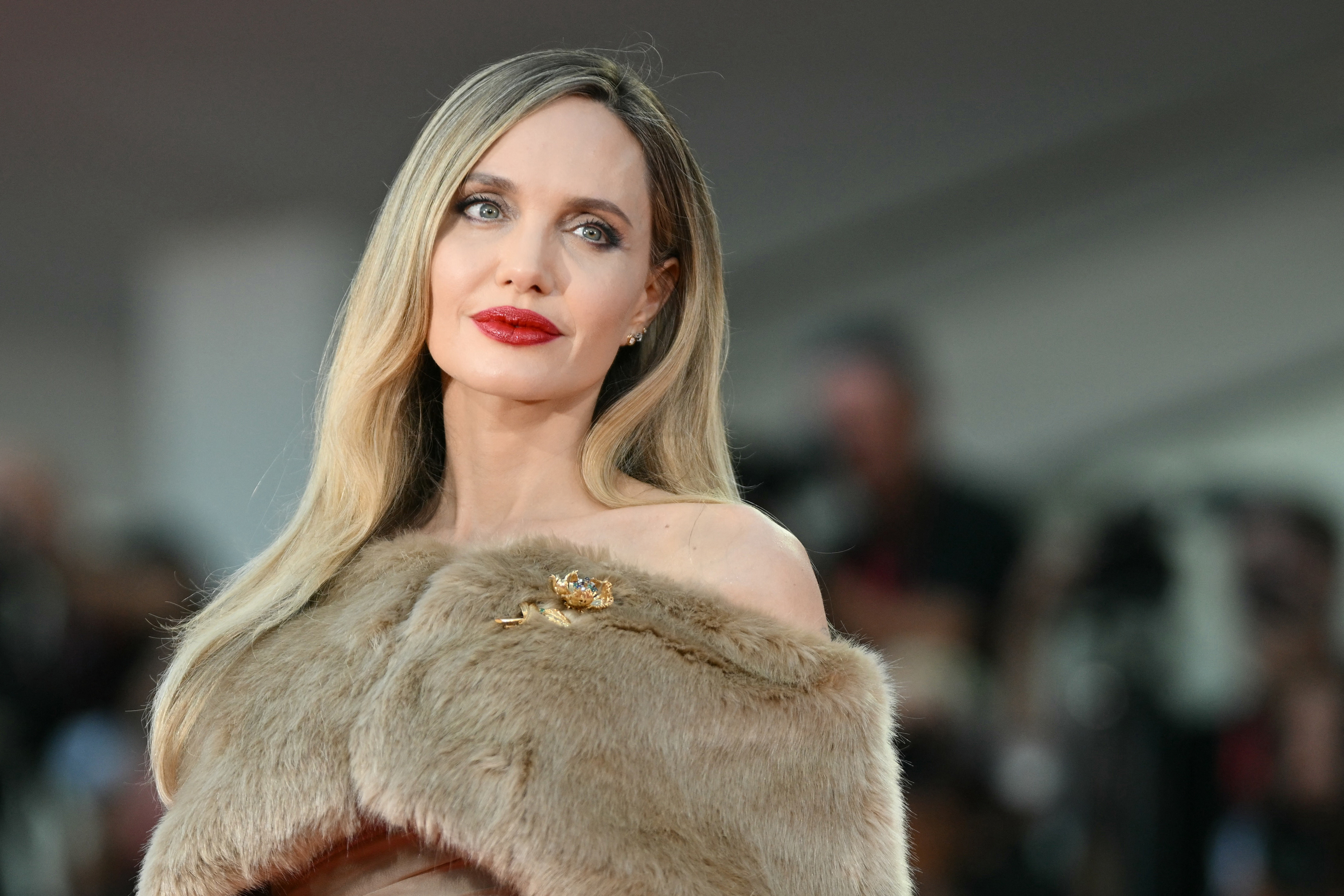 Angelina Jolie poses on a red carpet in an elegant off-shoulder outfit with a fur wrap