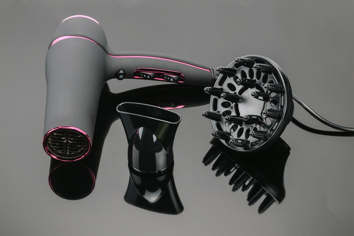 Modern hairdryer with two attachments, shown on a reflective surface for a beauty article; the attachments include a concentrator nozzle and a diffuser