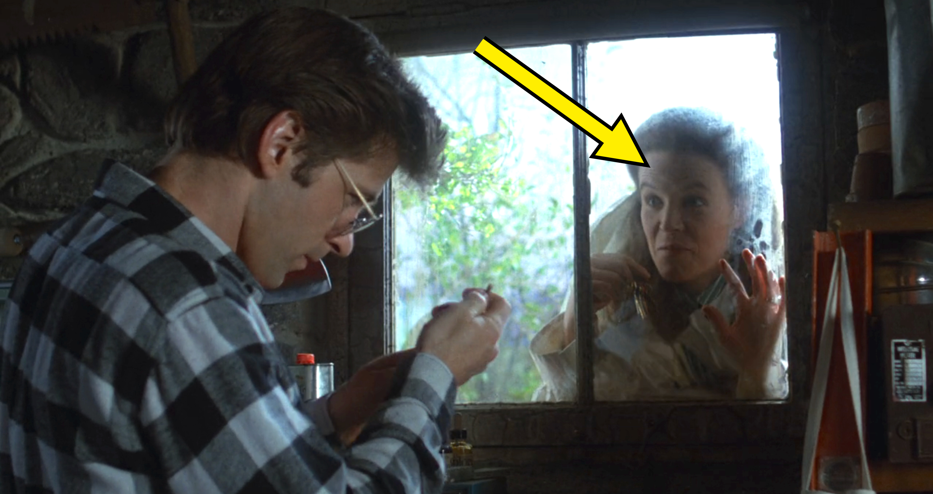 Alec Baldwin inspects a small item inside a workshop while his mother, Jane, looks concerned and presses her hands against the window