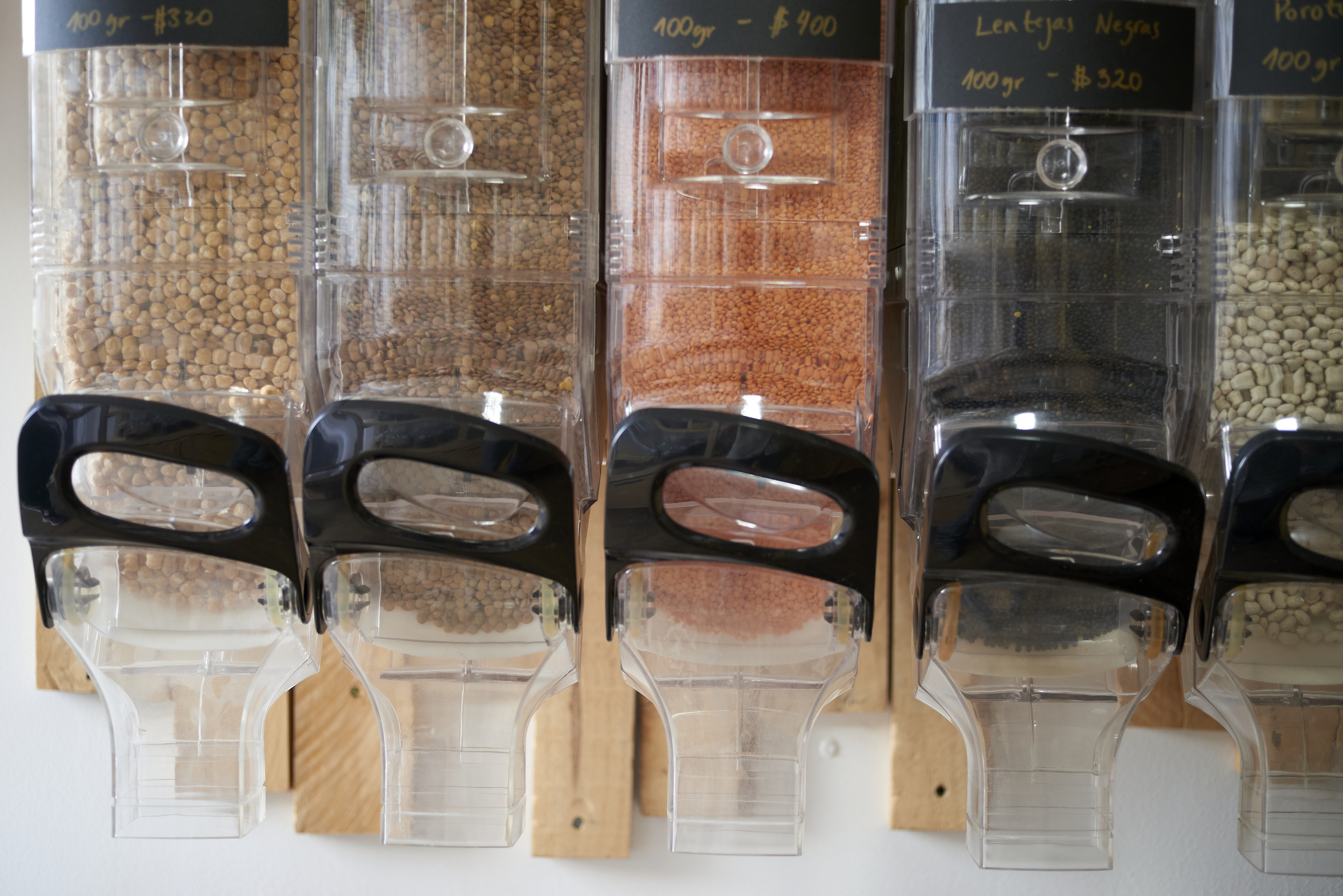 Five bulk food dispensers filled with different grains are arranged in a row. Labels with prices and types of grains are visible