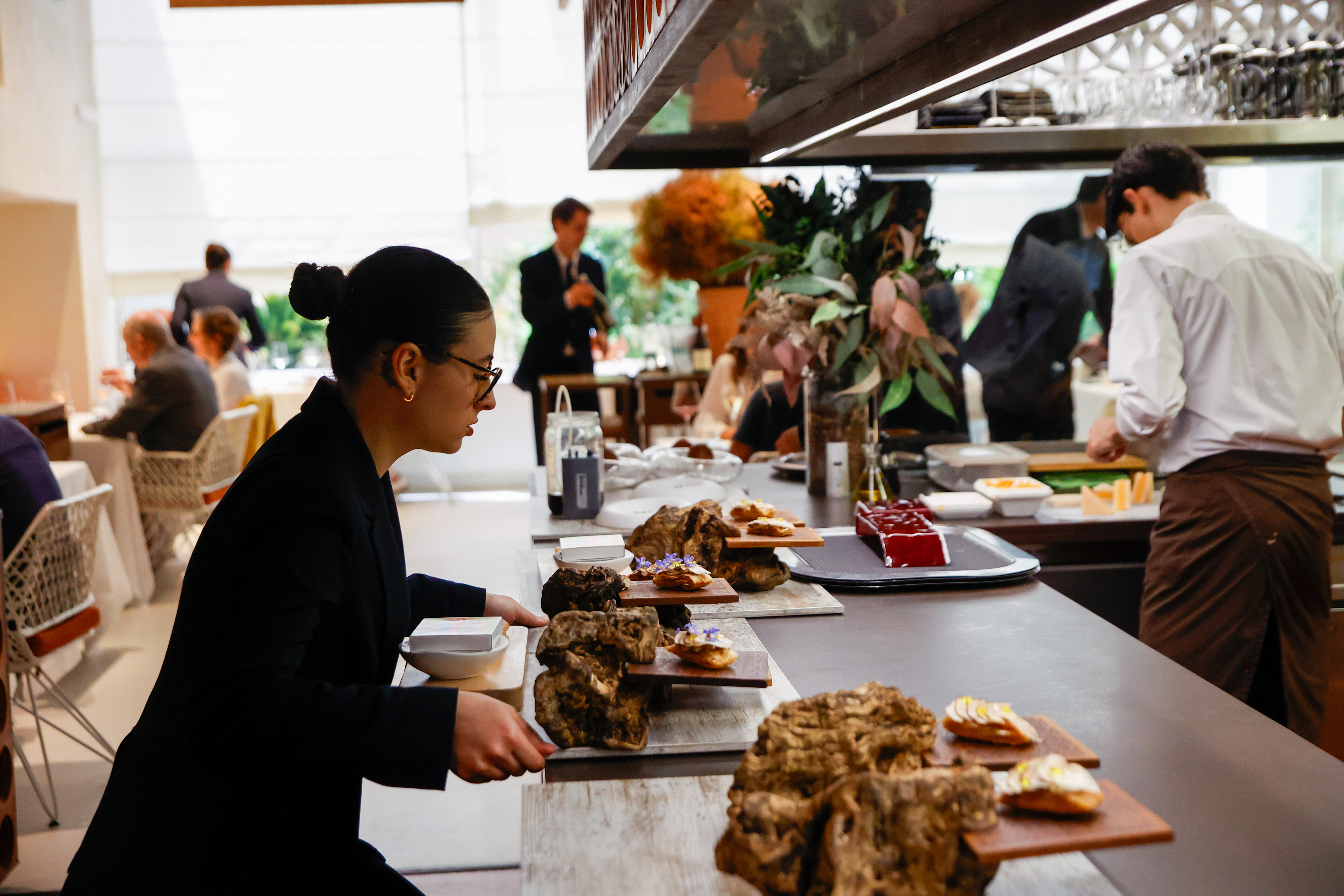 Restaurant staff serving appetizers as diners socialize and chefs prepare dishes in the background