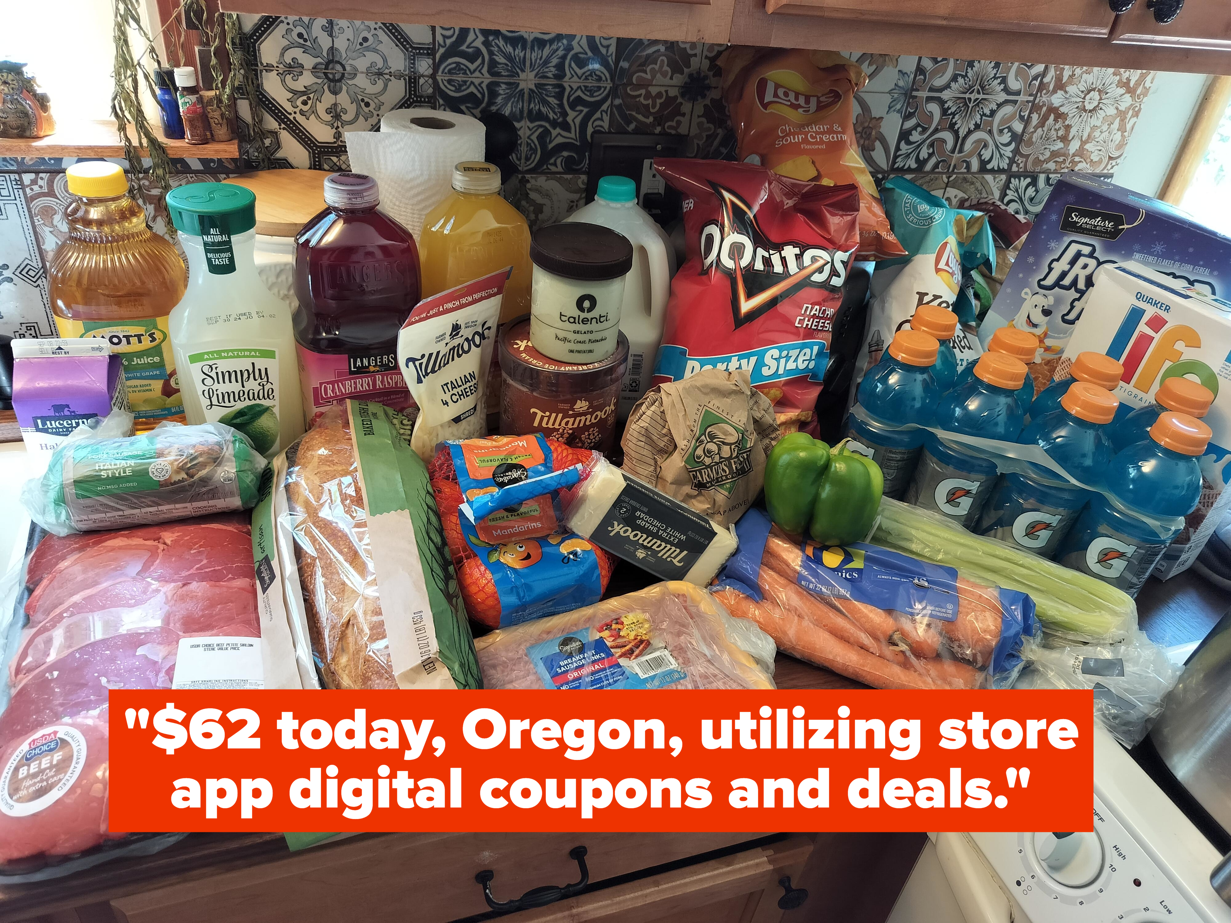 A kitchen counter laden with various groceries, including juices, chips, bread, meats, vegetables, snacks, and sports drinks