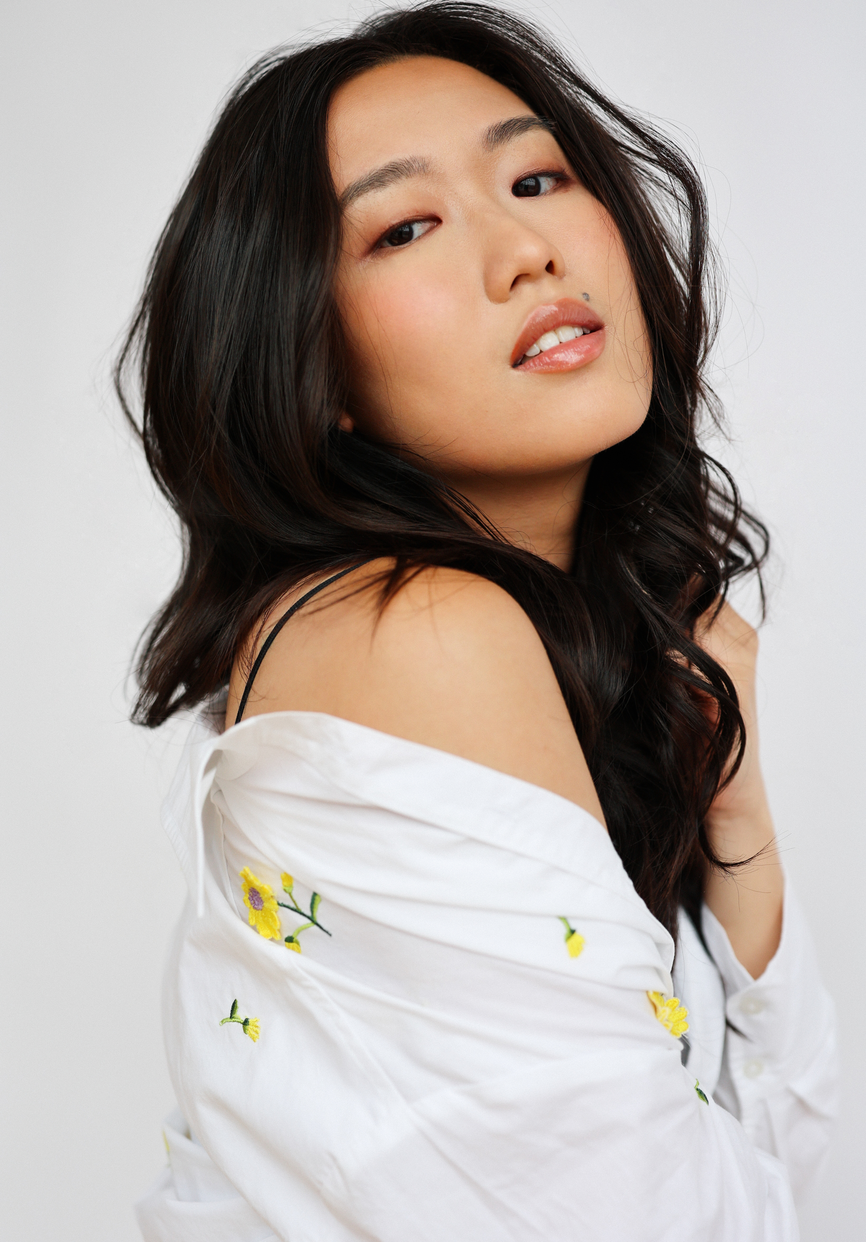 Woman in a white off-shoulder top with floral embroidery, looking over her shoulder with her hair styled in loose waves
