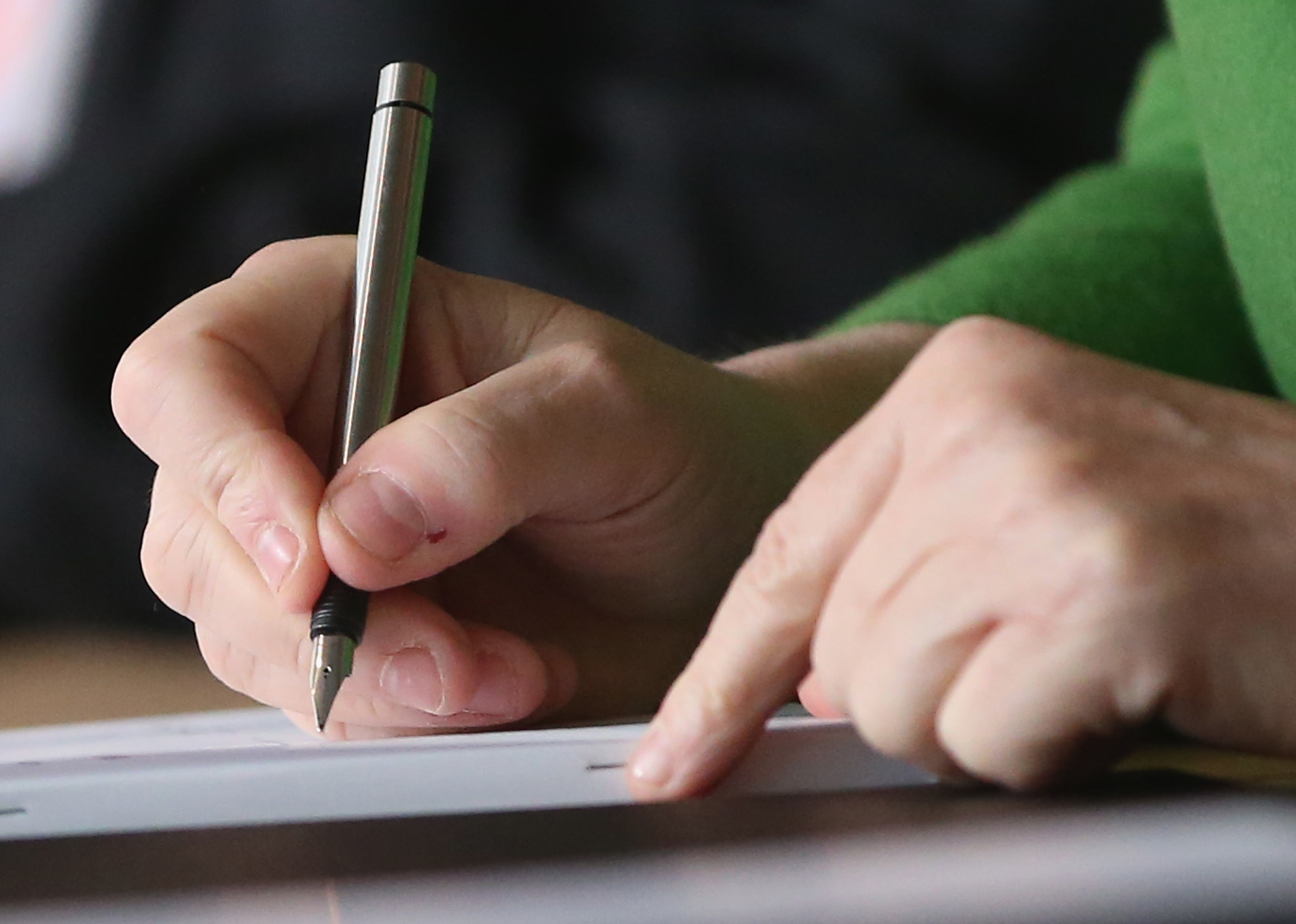 A close-up of a person holding a pen and pointing to a piece of paper. The person's hands are the focus of the image