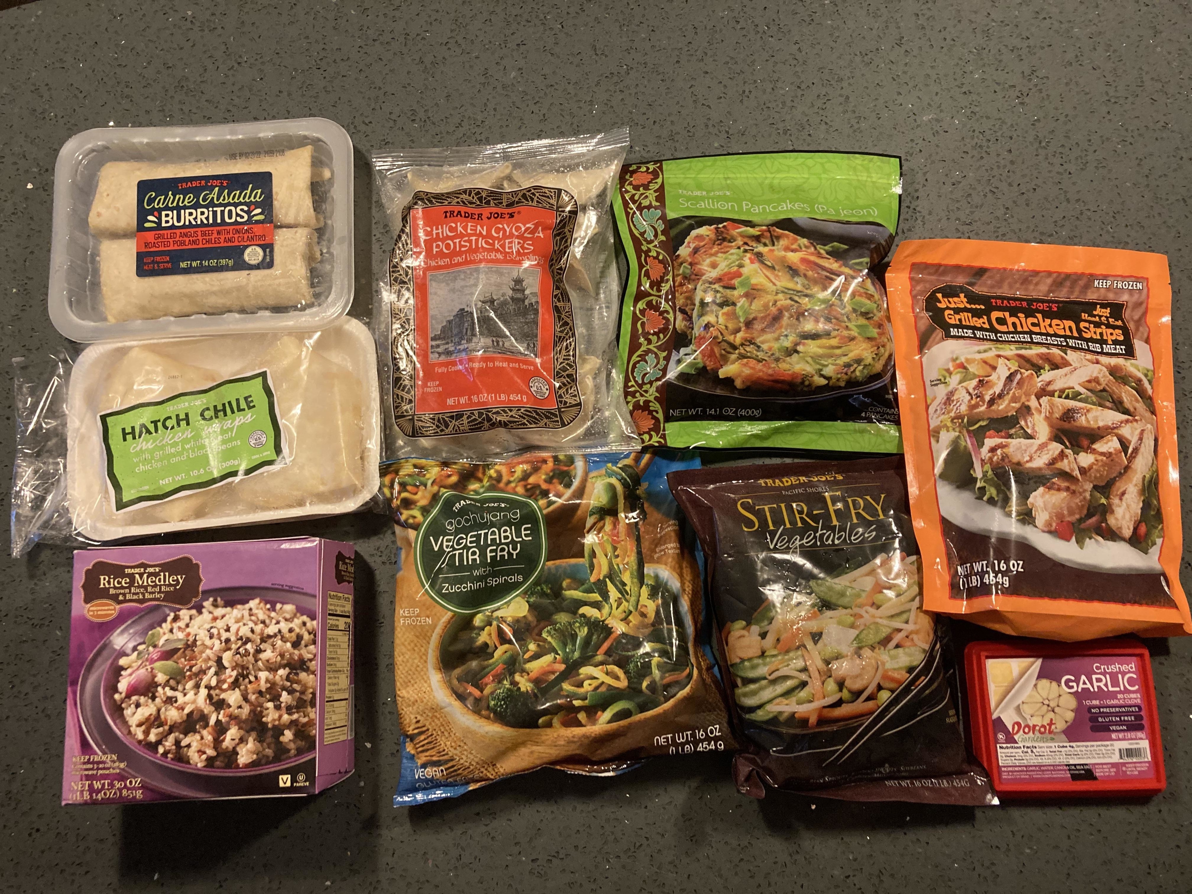 A variety of frozen and prepackaged foods are arranged on a countertop, including burritos, potstickers, vegetable medley, vegetable stir-fry, and chicken strips