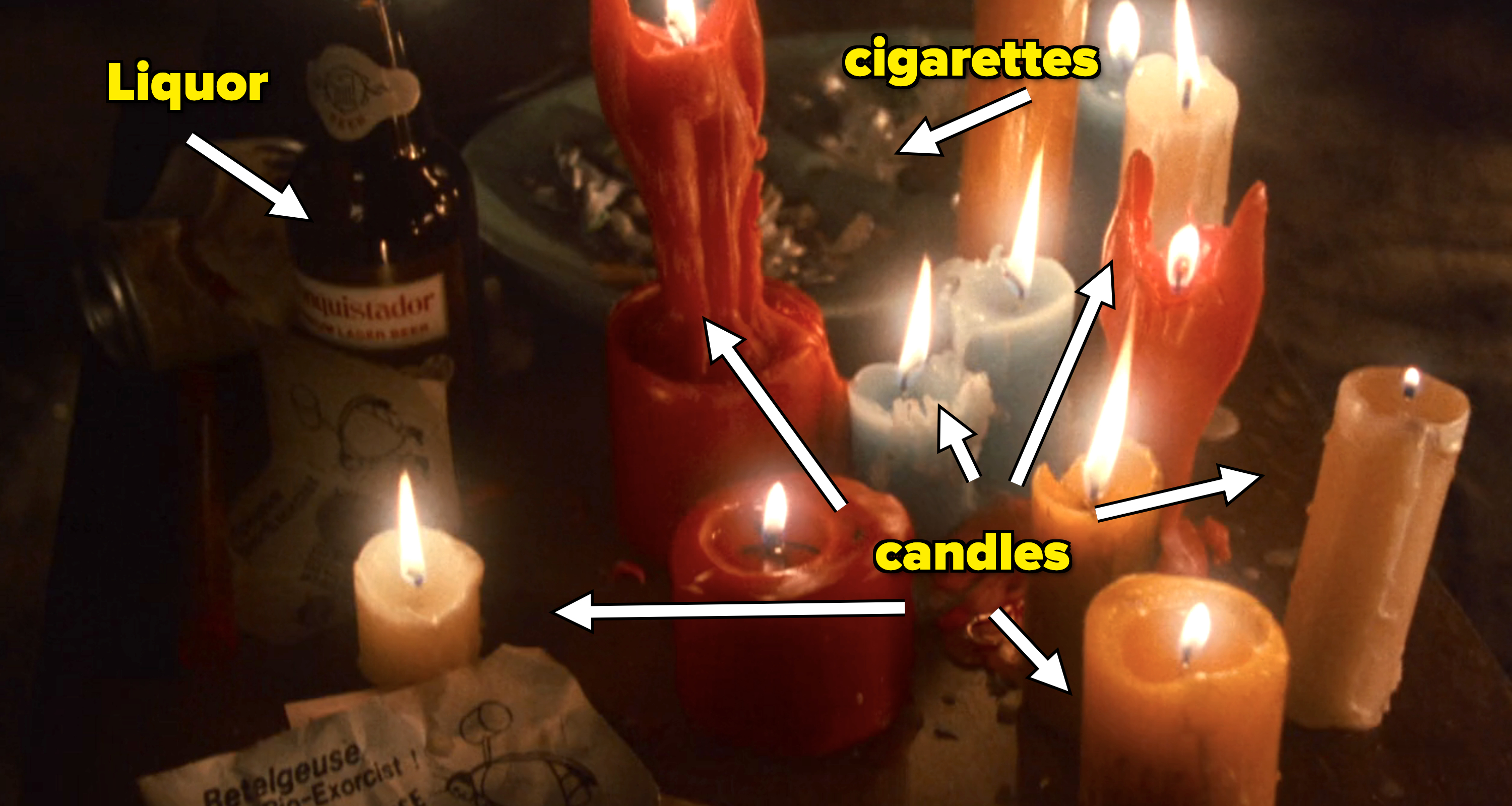 Various lit candles, some with melted wax drippings, surround an open bottle and scattered wrappers on a dark surface