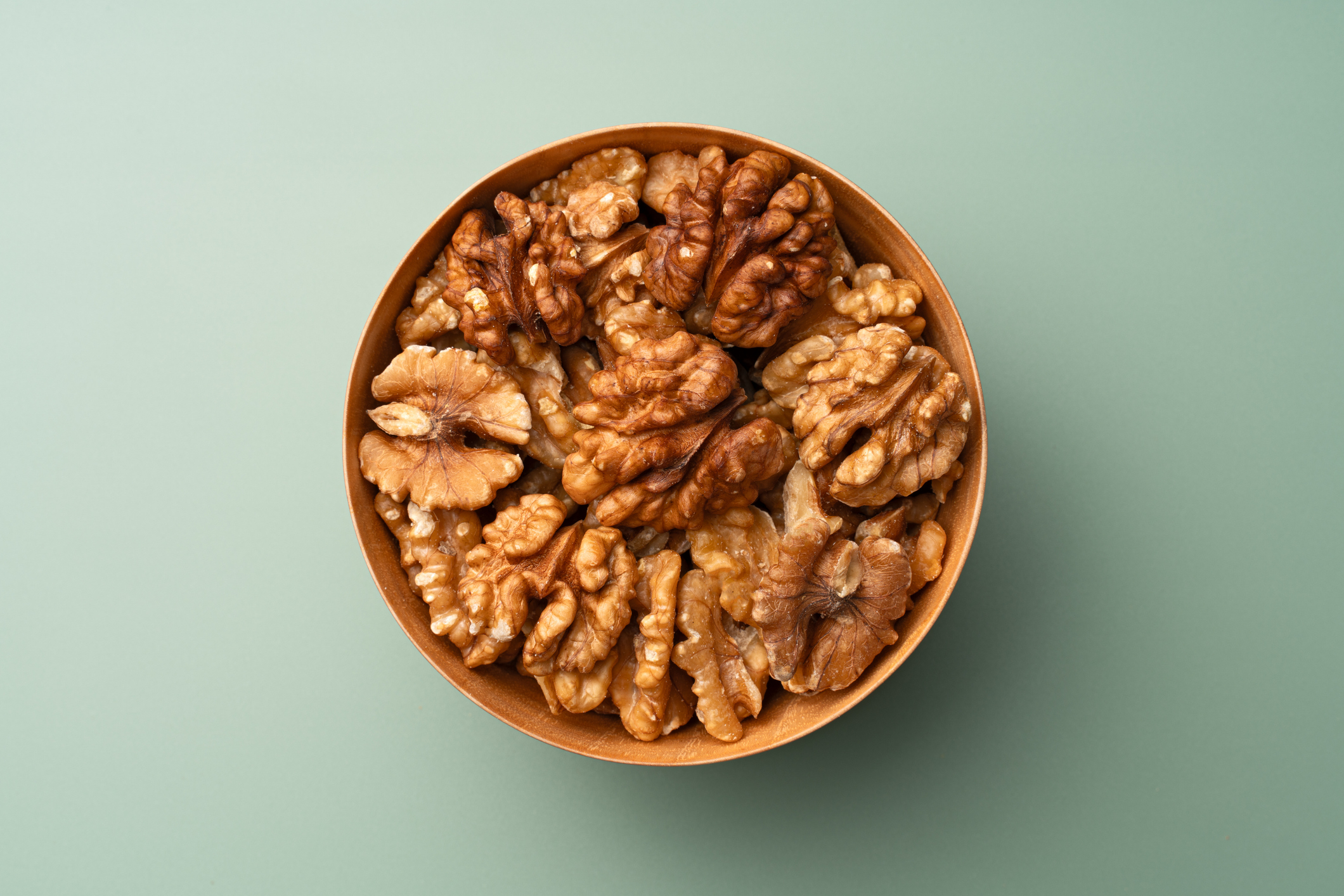 A bowl filled with shelled walnut halves on a plain surface