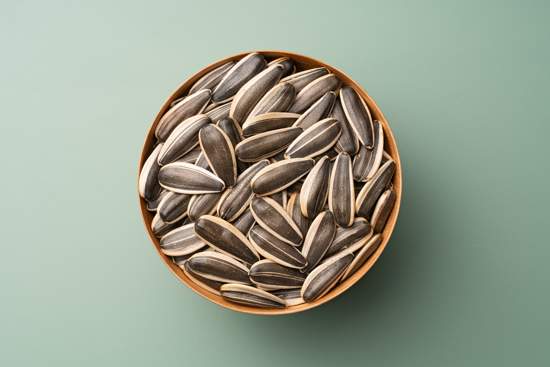 A bowl filled with sunflower seeds on a flat surface
