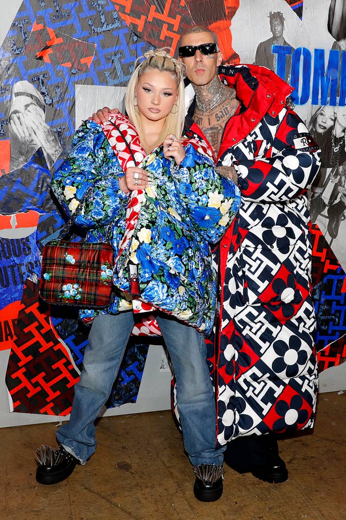 Alabama Barker, in a floral quilted jacket and jeans, poses with Travis Barker, in a patterned oversized coat, against a vibrant patterned backdrop