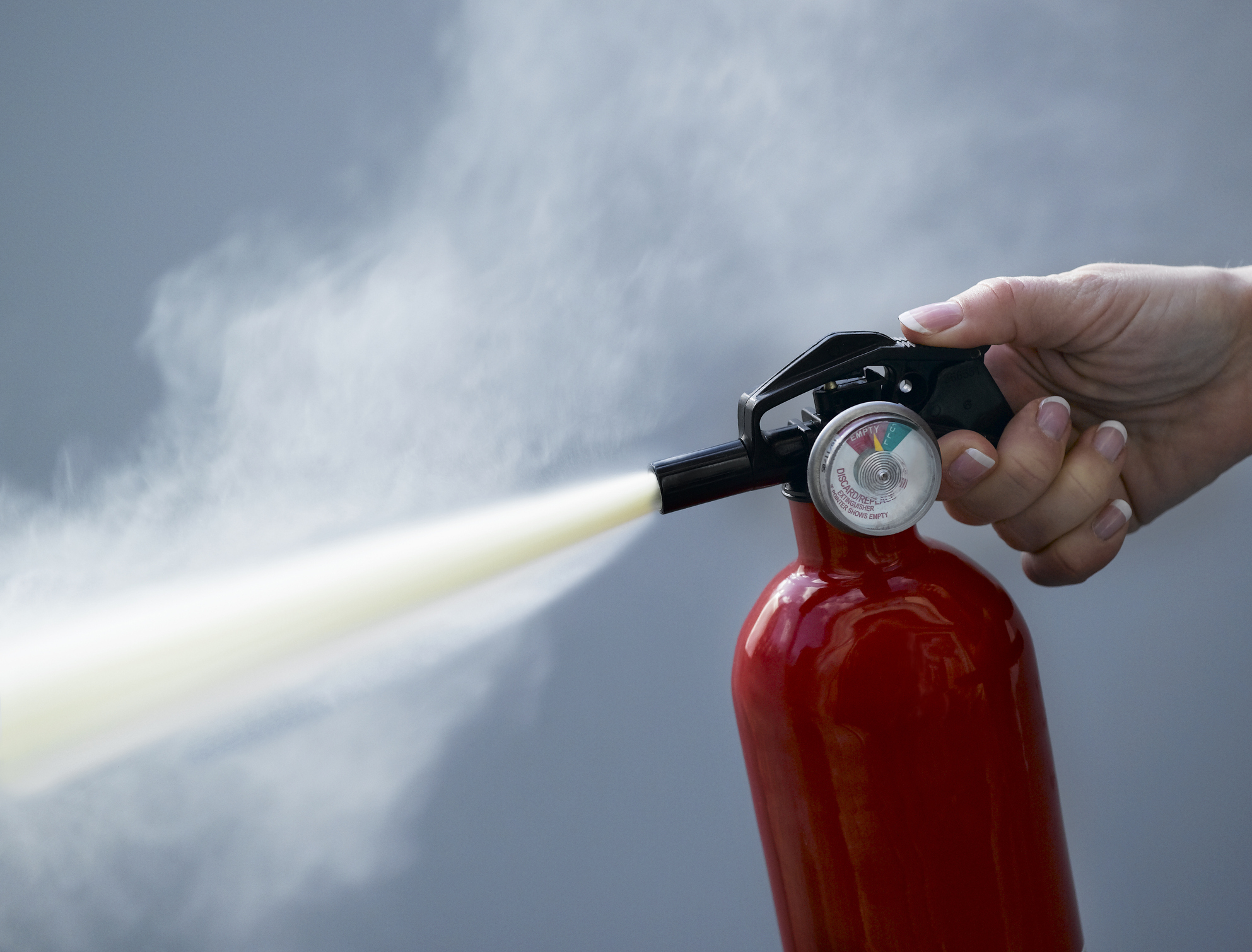 A hand holding and discharging a red fire extinguisher, with white spray coming out