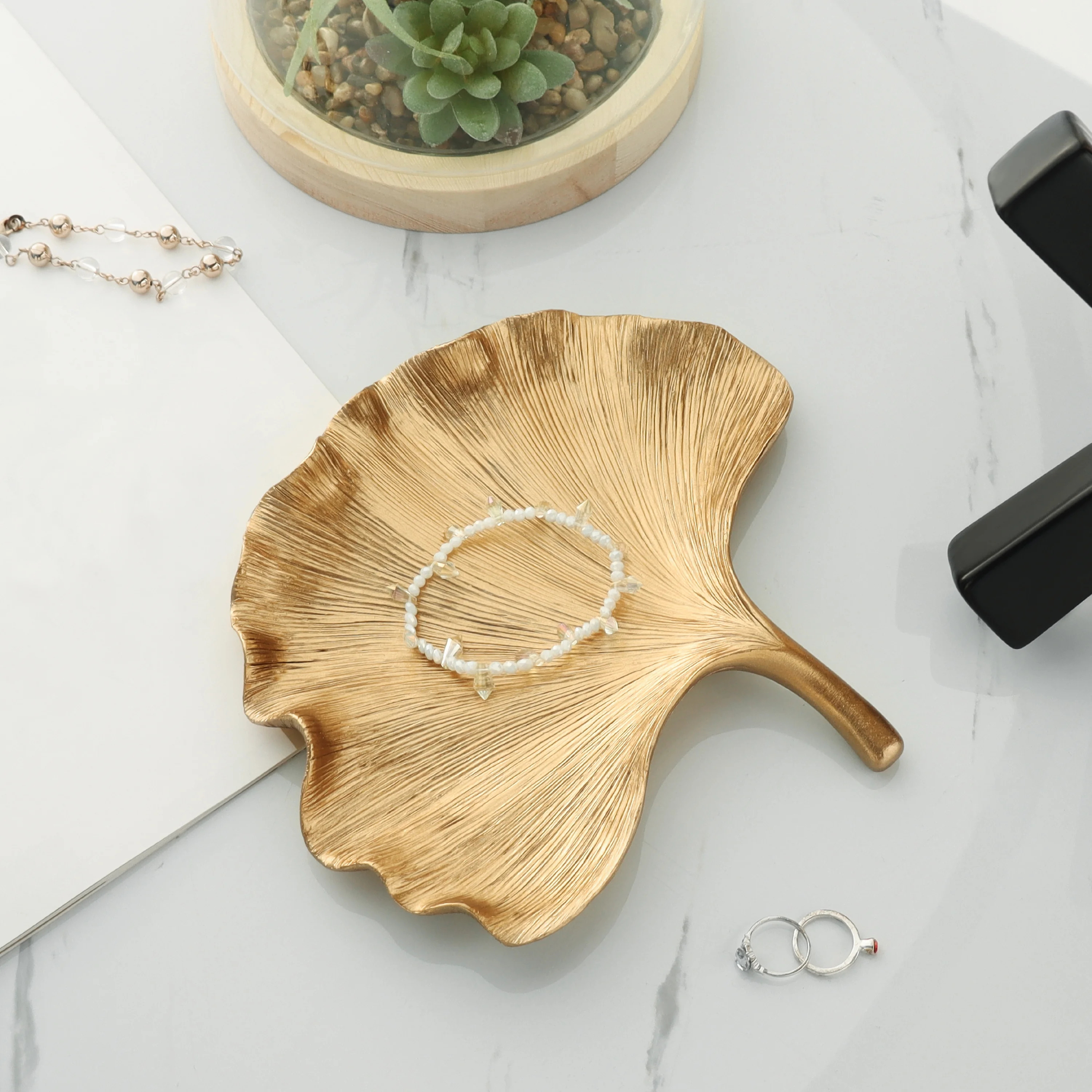 A golden leaf-shaped tray holds a pearl bracelet