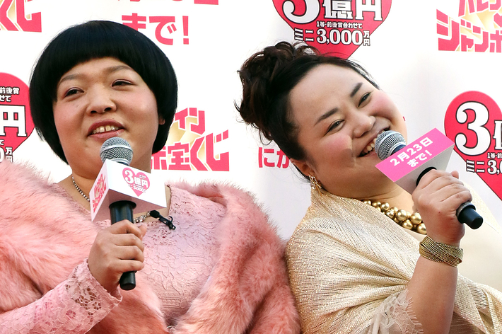 女性二人がバレンタインジャンボ宝くじのイベントでマイクを持ってポーズを取っています。