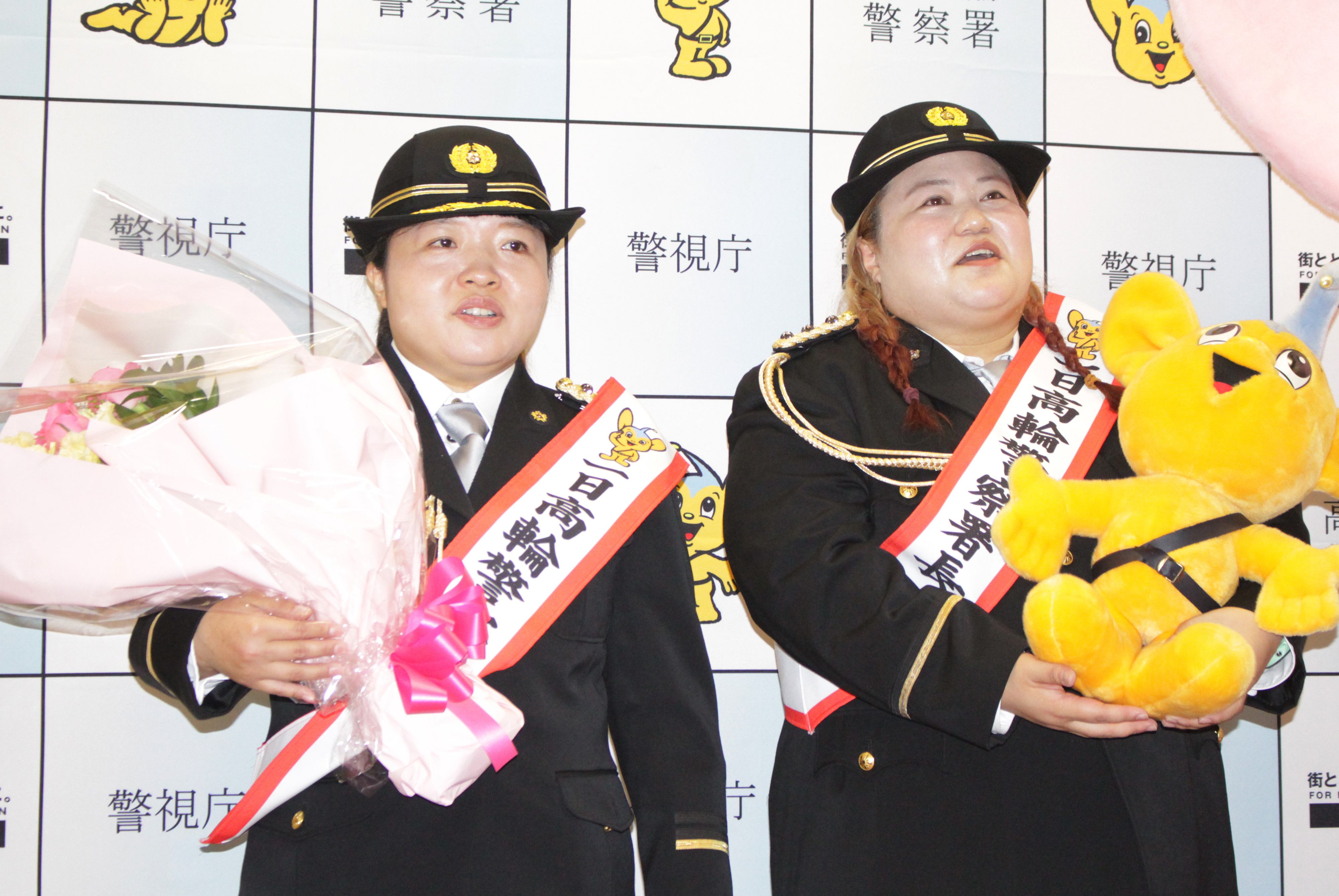 バナナマン日村勇紀と設楽統が警視庁の制服を着て表彰式に出席しています。日村は花束を、設楽は黄色いぬいぐるみを持っています。