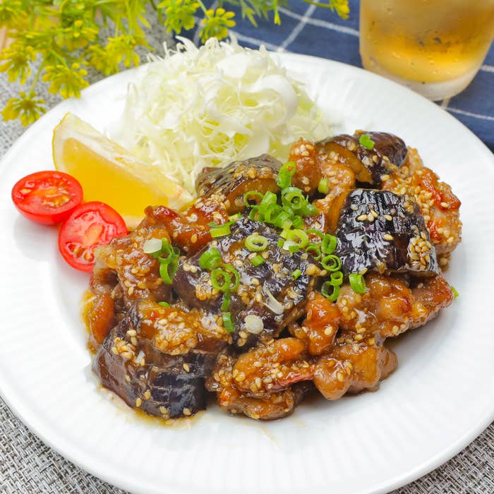 皿に盛られた茄子と肉の炒め物、付け合わせにキャベツ、レモン、ミニトマトが添えられている料理。