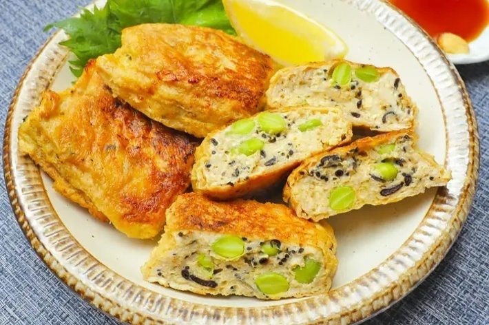 皿に盛られた枝豆と黒ゴマが入った卵焼き、レモンの角切り付き。酢醤油が小皿に入っている。