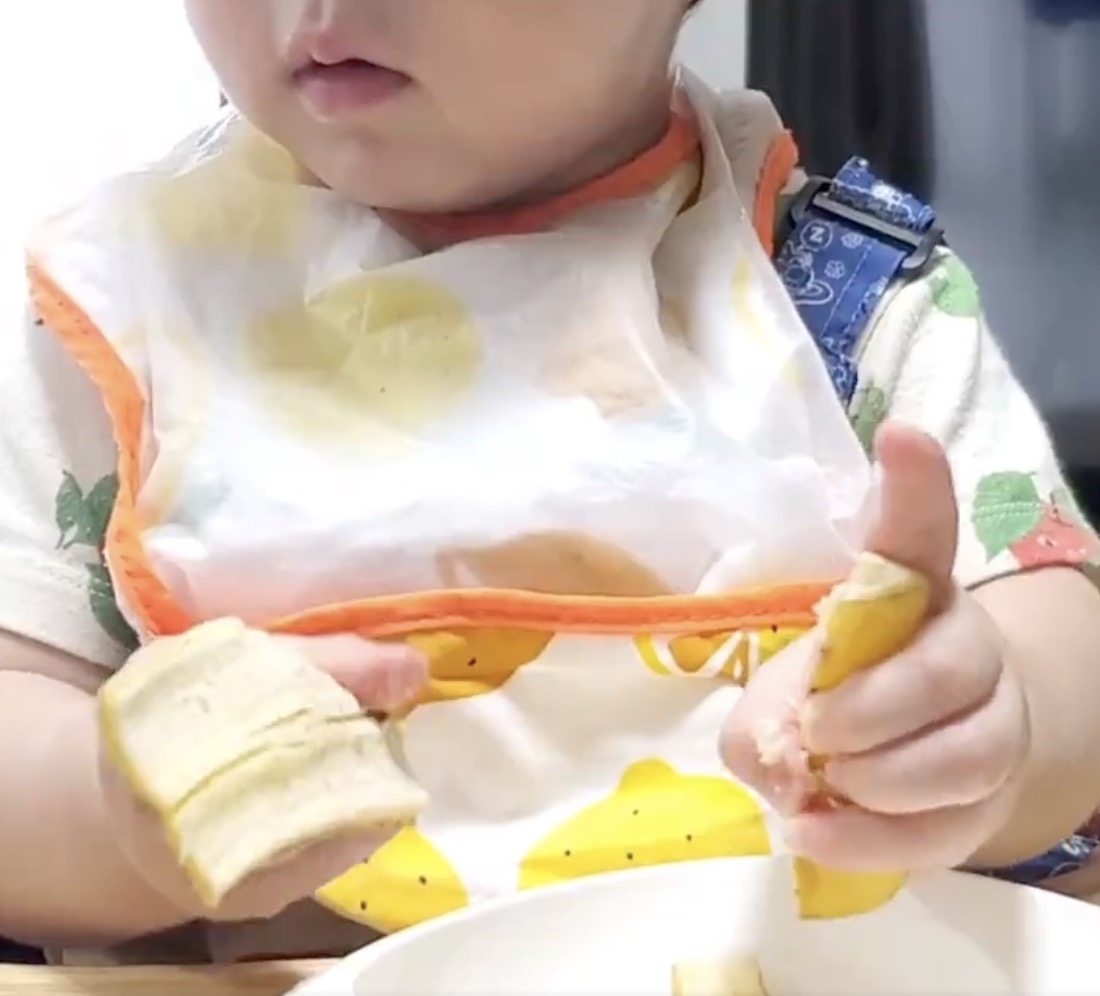 幼児がバナナの断片を両手に持ち、口元に近づけているシーン。