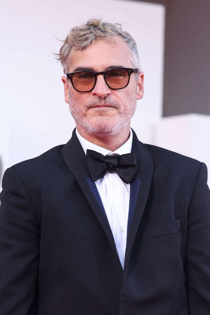 Joaquin Phoenix on the red carpet wearing a formal black tuxedo with a bow tie and sunglasses