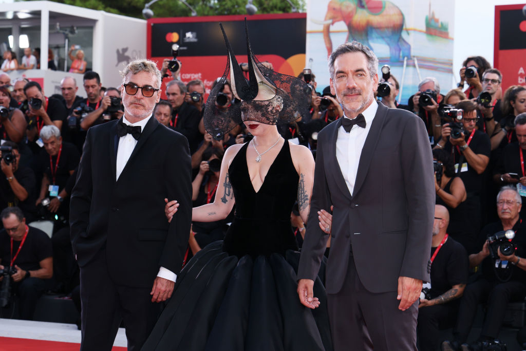 Joaquin Phoenix, Lady Gaga in a dramatic gown with headpiece, and Todd Phillips pose at a red-carpet event