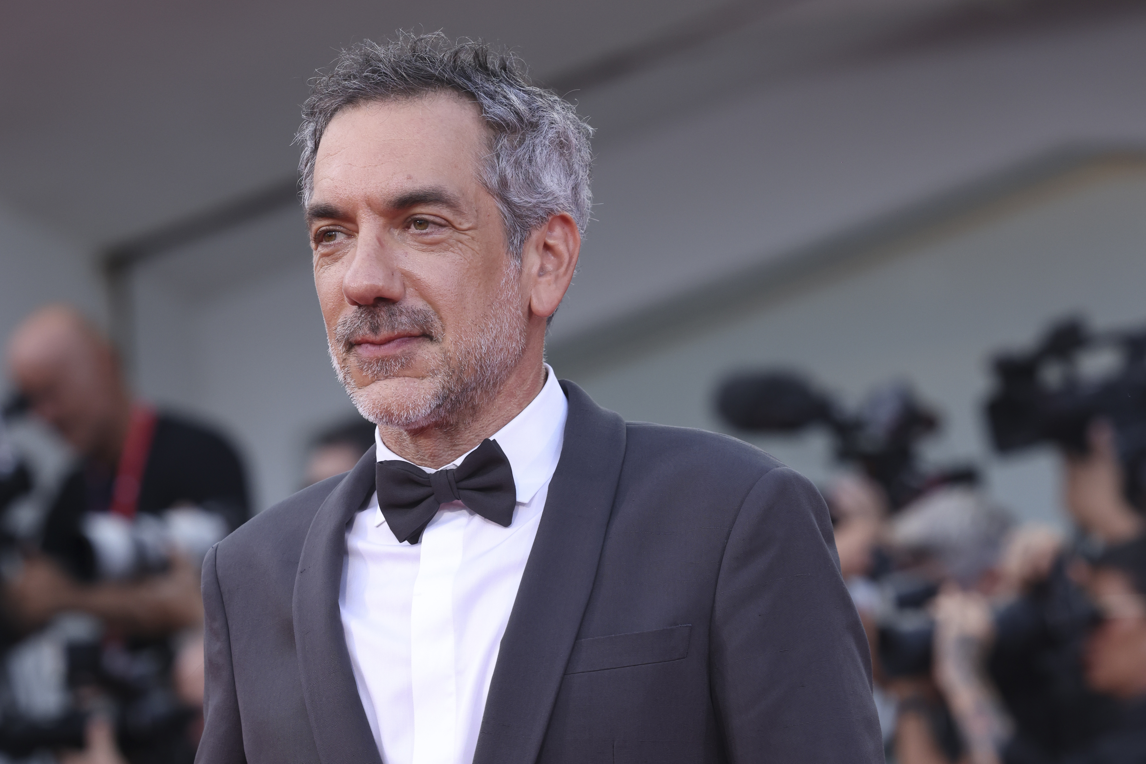 Todd phillips in a tuxedo with a black bowtie stands on the red carpet, photographers in the background