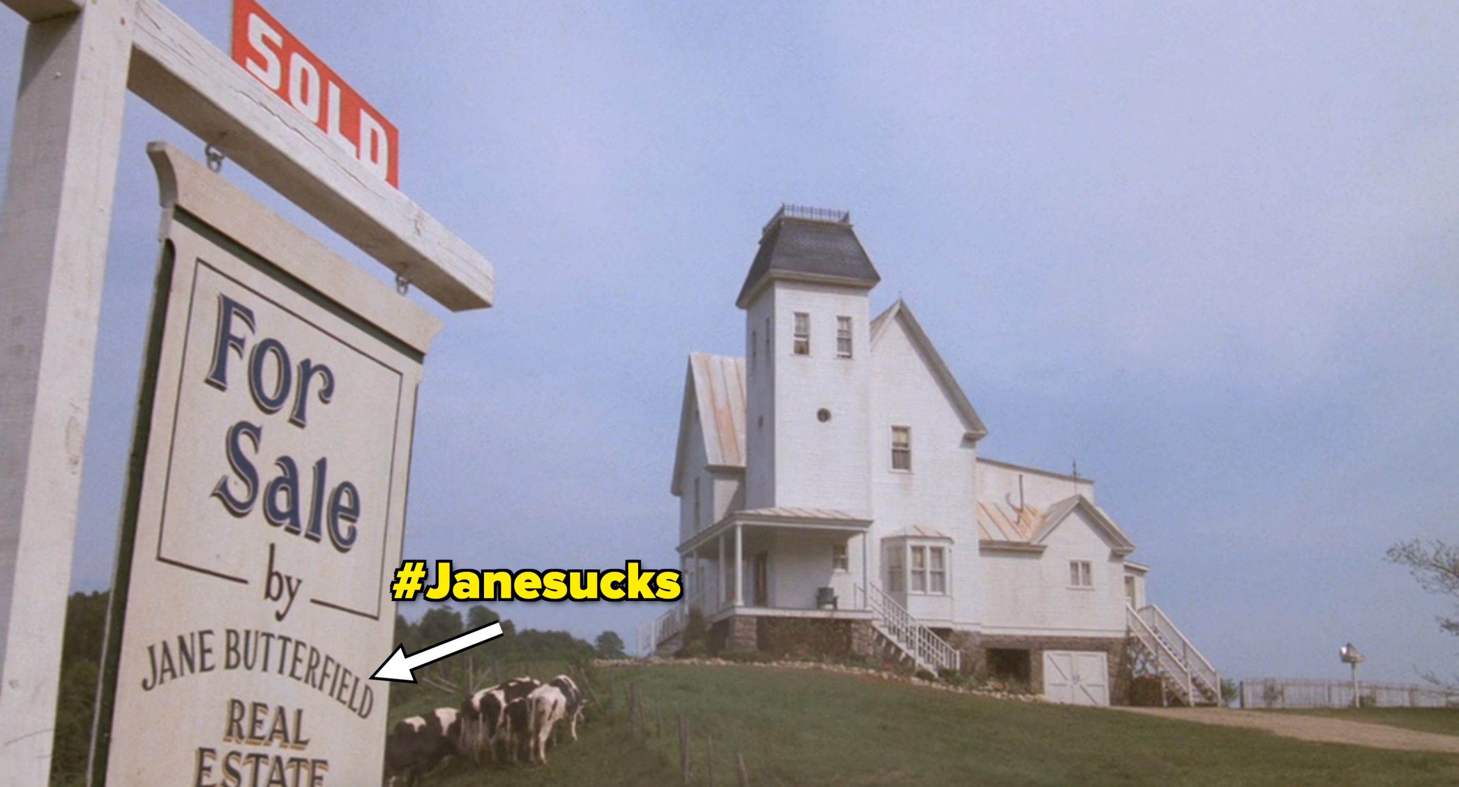 A "Sold" sign in front of a white, multi-story house with a distinctive tower and cows grazing nearby. The sign reads "For Sale by Jane Butterfield Real Estate." in "Beetlejuice"