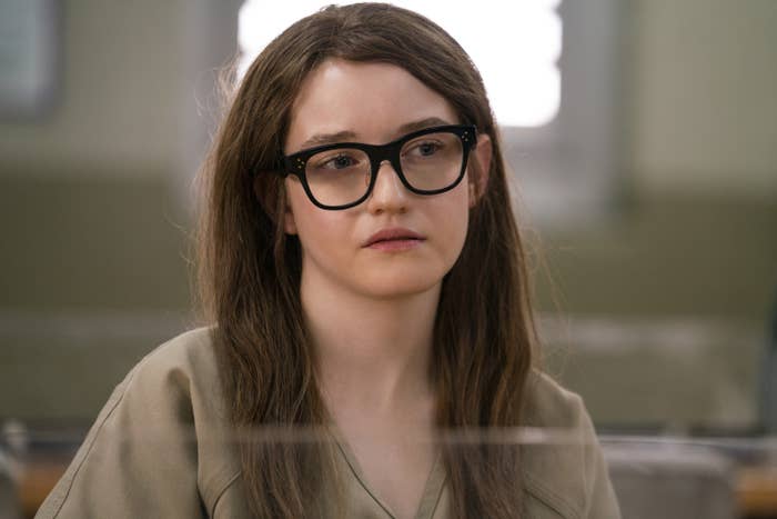 Julia Garner, portraying a character from the TV series &quot;Inventing Anna,&quot; wears black glasses and a prison uniform, looking pensive