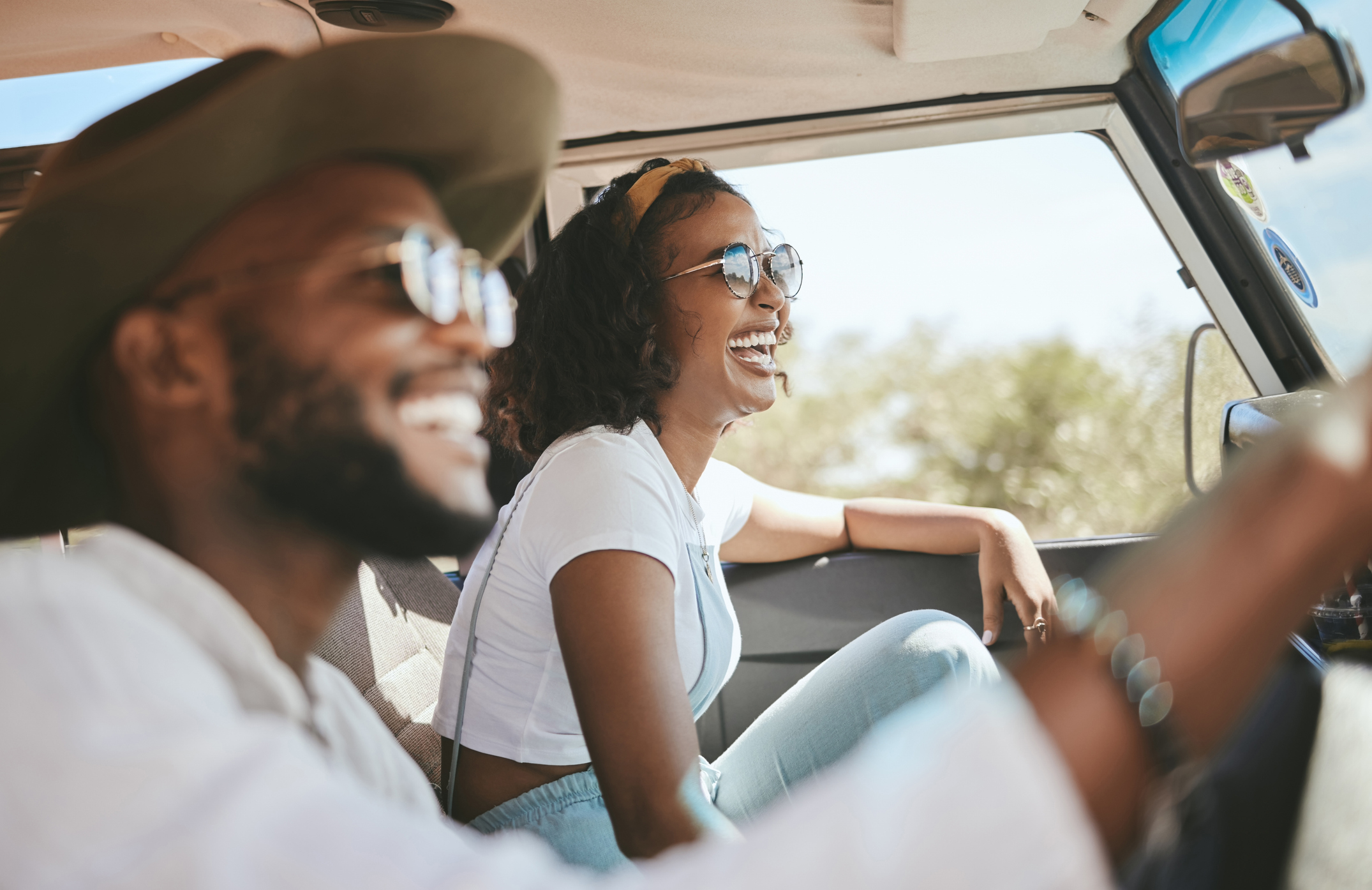Man and woman smiling and laughing while sitting inside a car, possibly on a road trip