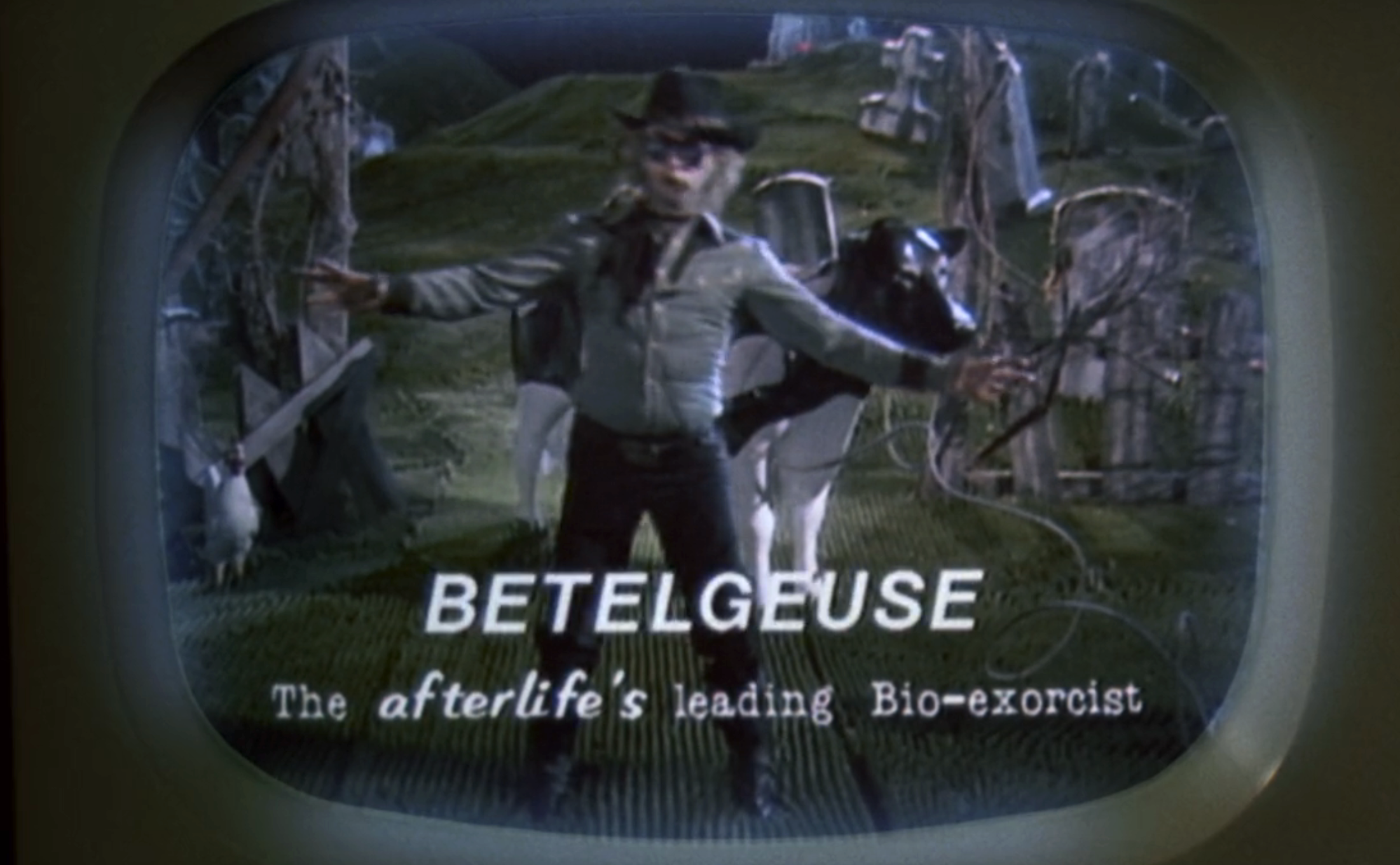 Betelgeuse on TV screen, wearing a hat and a jacket, advertising himself as "the afterlife's leading Bio-exorcist."
