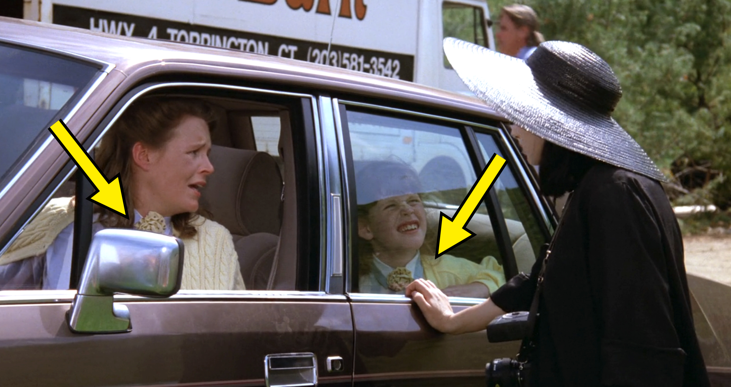 Jane and a child in a car are talking to Winona Ryder wearing a large hat. They appear to be having an animated conversation