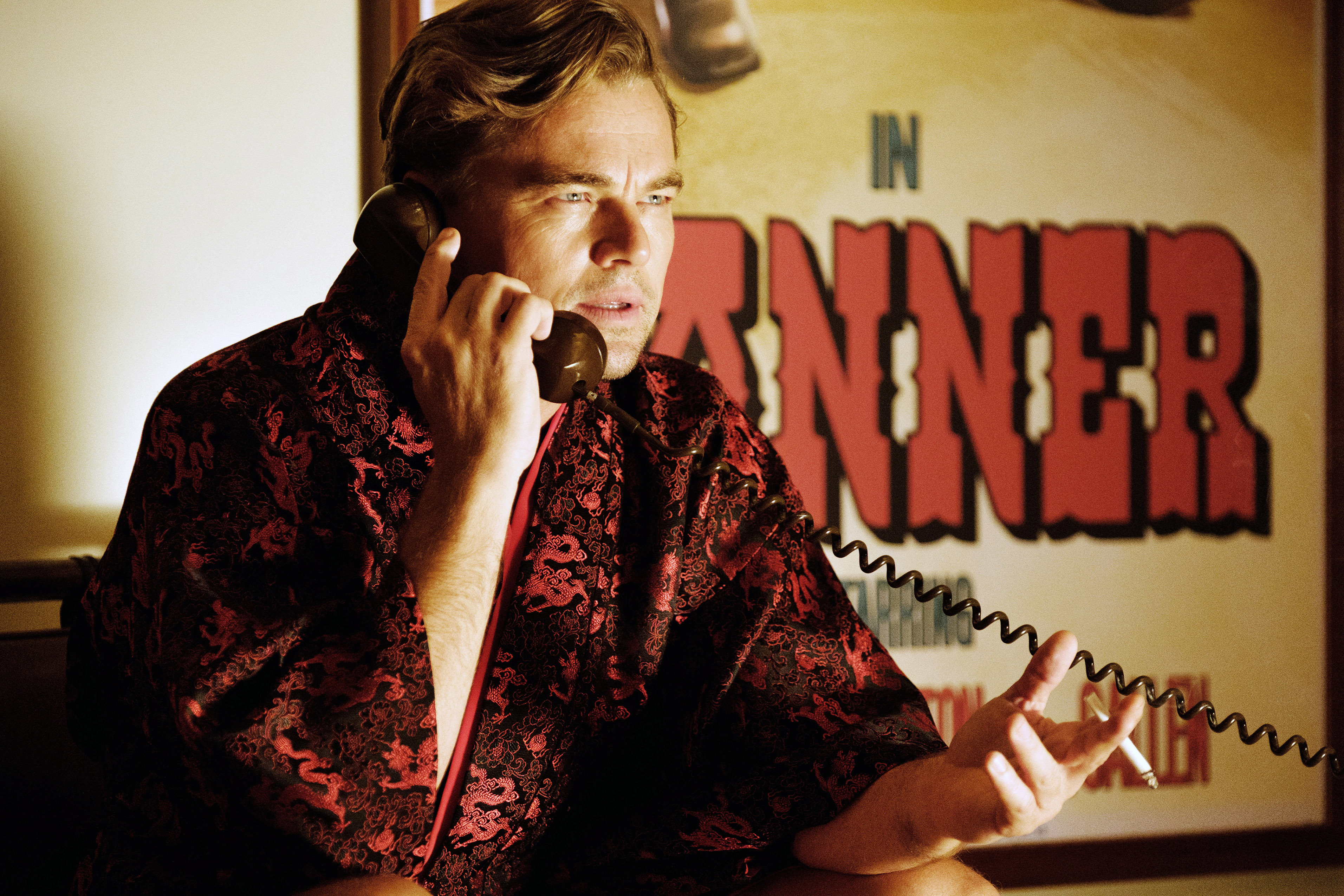 Leonardo DiCaprio in a patterned robe talking on the phone, sitting in front of a movie poster