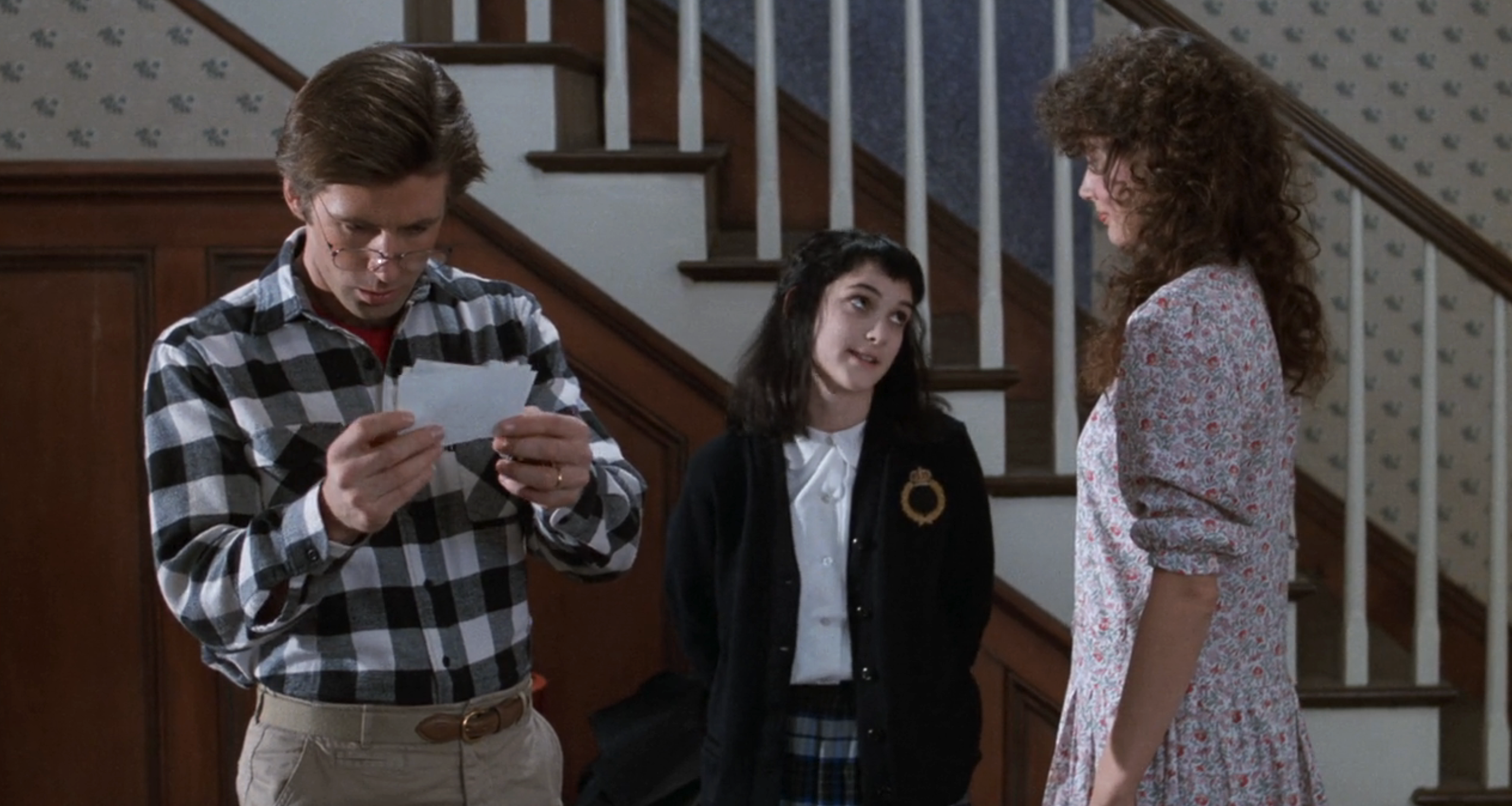 Alec Baldwin examines papers near Winona Ryder and Geena Davis standing on a staircase. Ryder looks up at Baldwin; Davis wears a floral dress